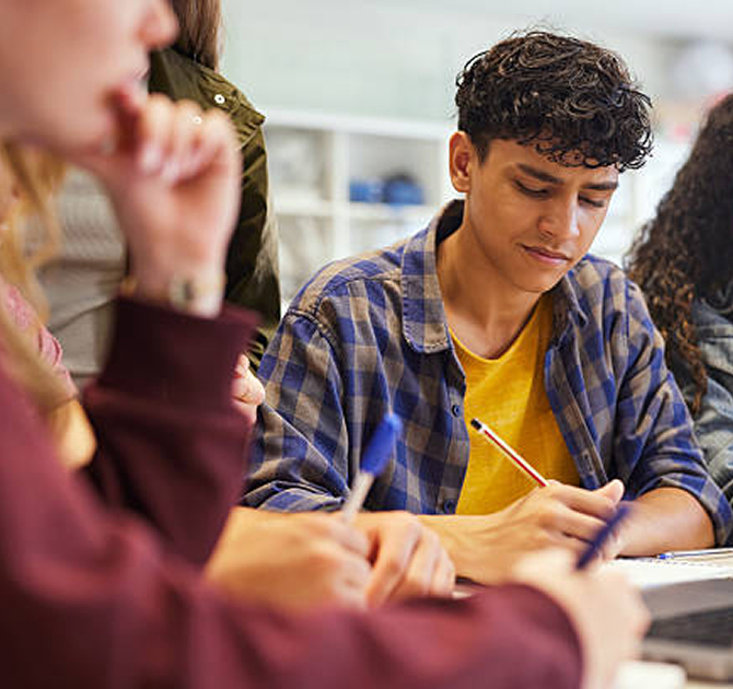 Respire Education | Student in a plaid shirt writing with a pencil in a classroom.