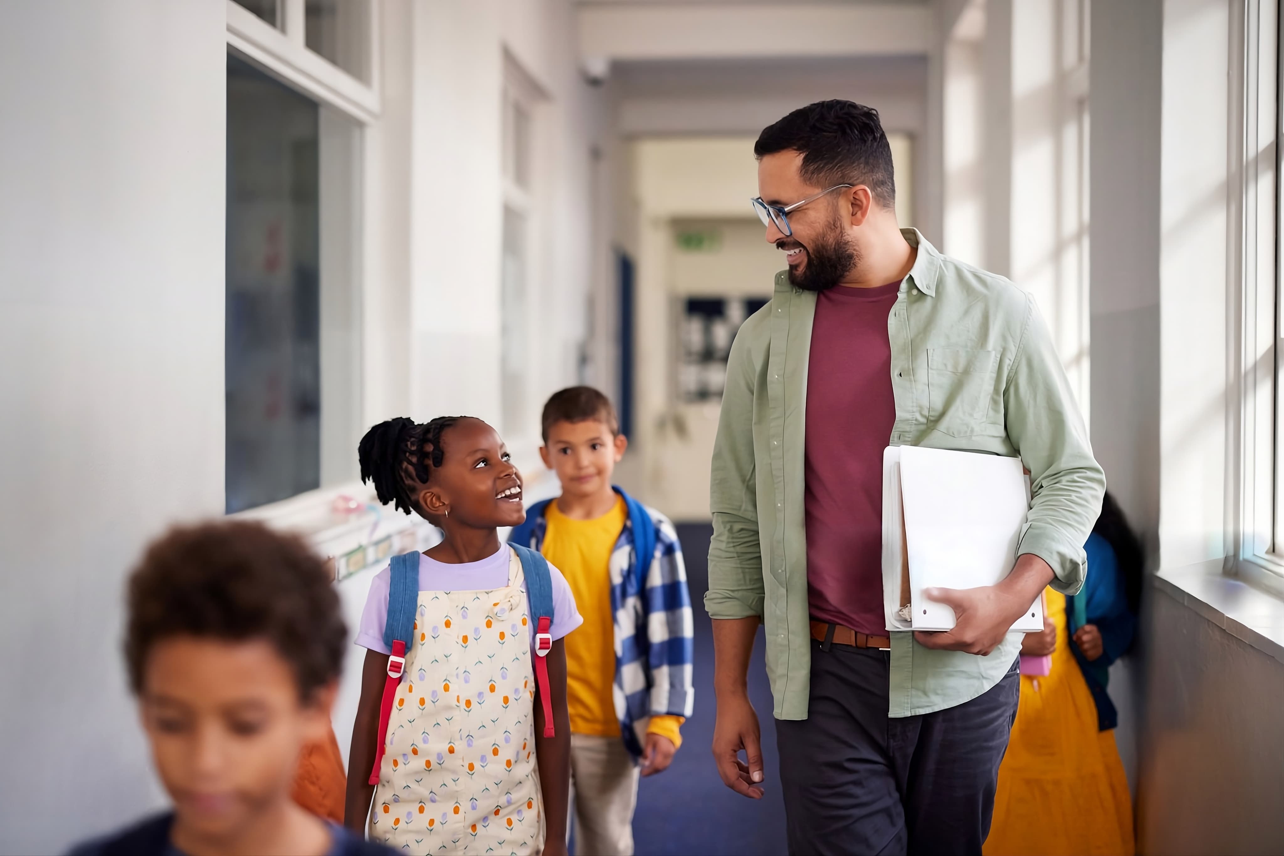 Respire Education | Smiling male teacher walking and talking with happy schoolchildren in a hallway.