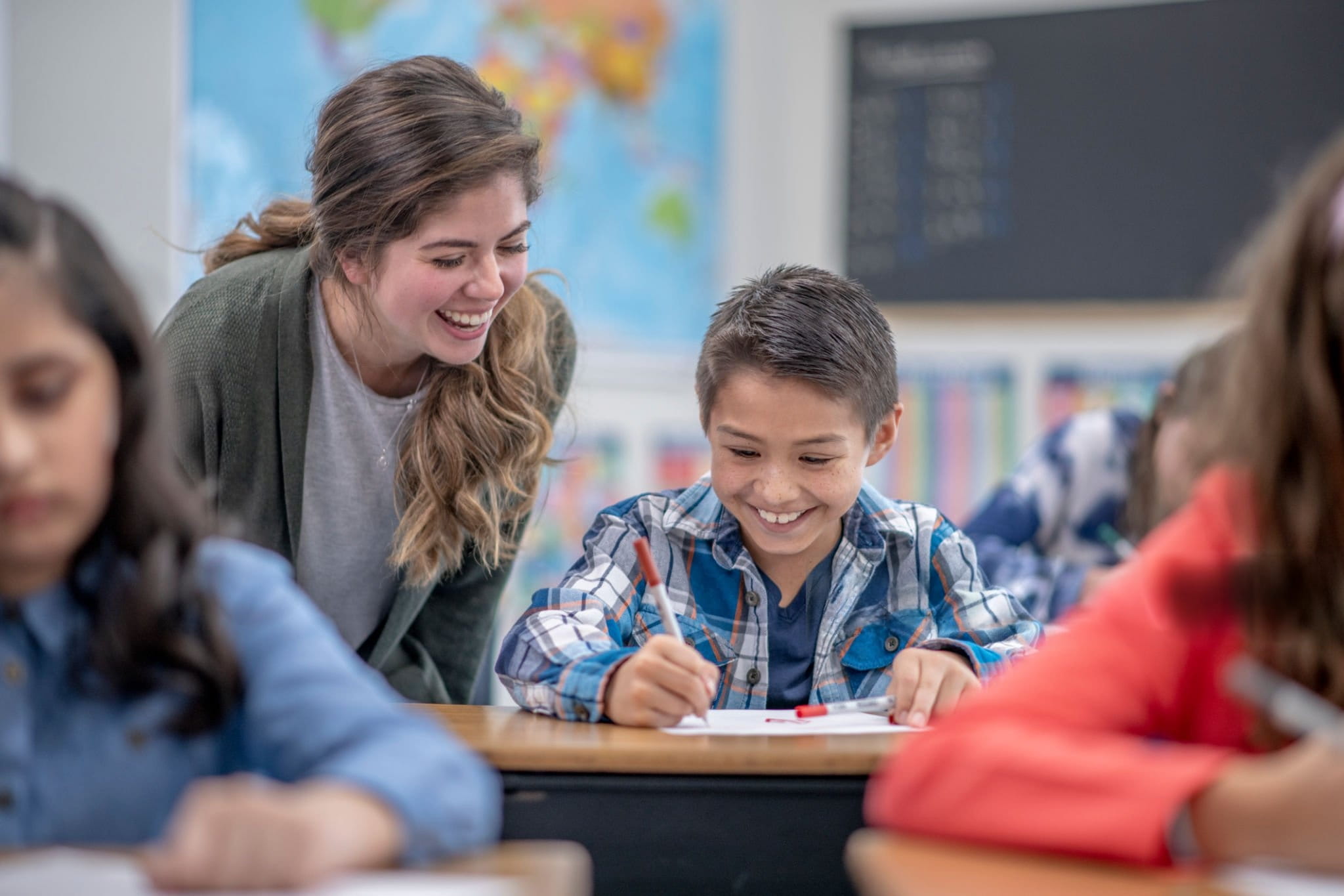 Respire Education | Teacher smiling and assisting a boy writing at his desk in a classroom.
