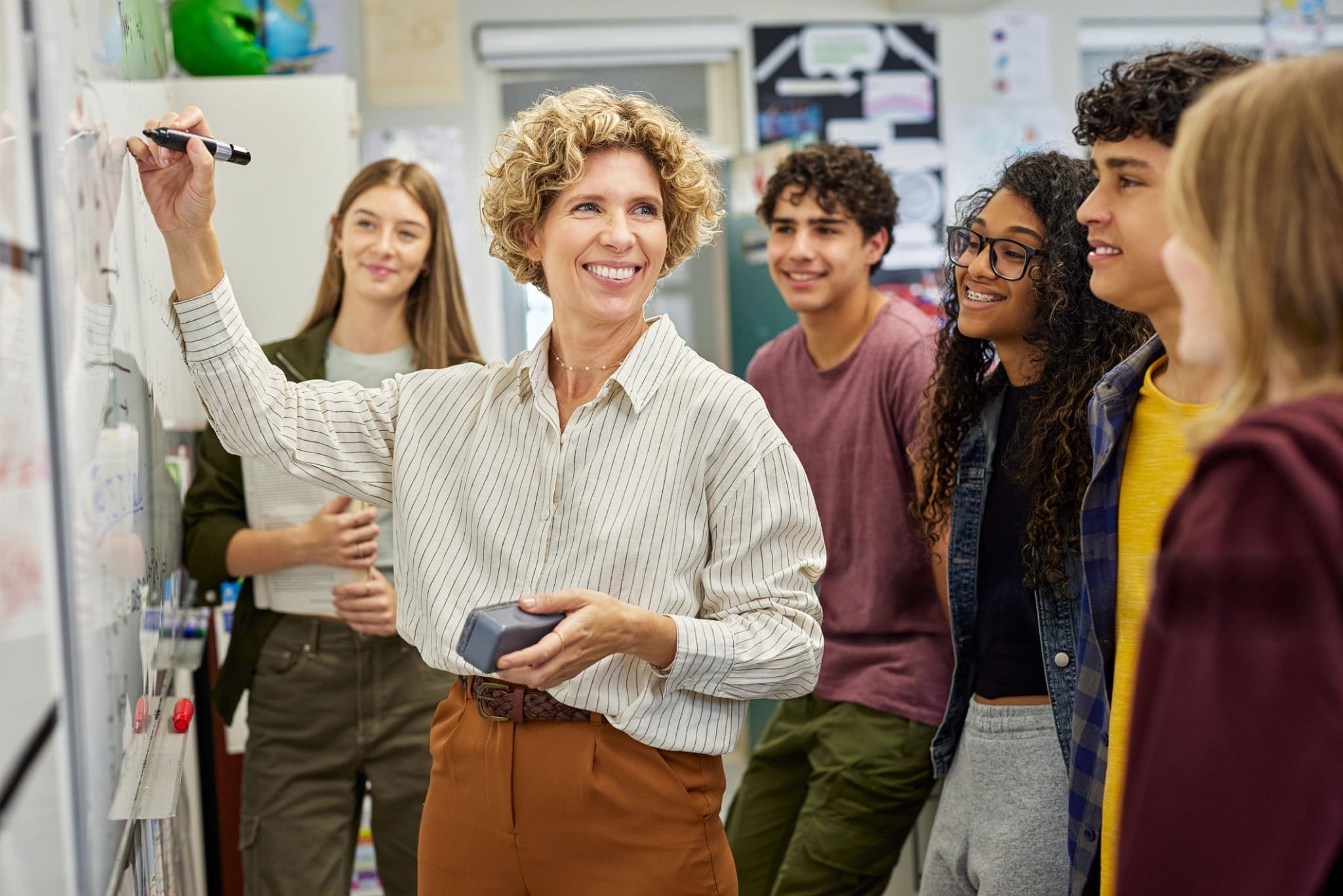 Respire Education | Teacher smiling and writing on a whiteboard while students watch attentively in a classroom.