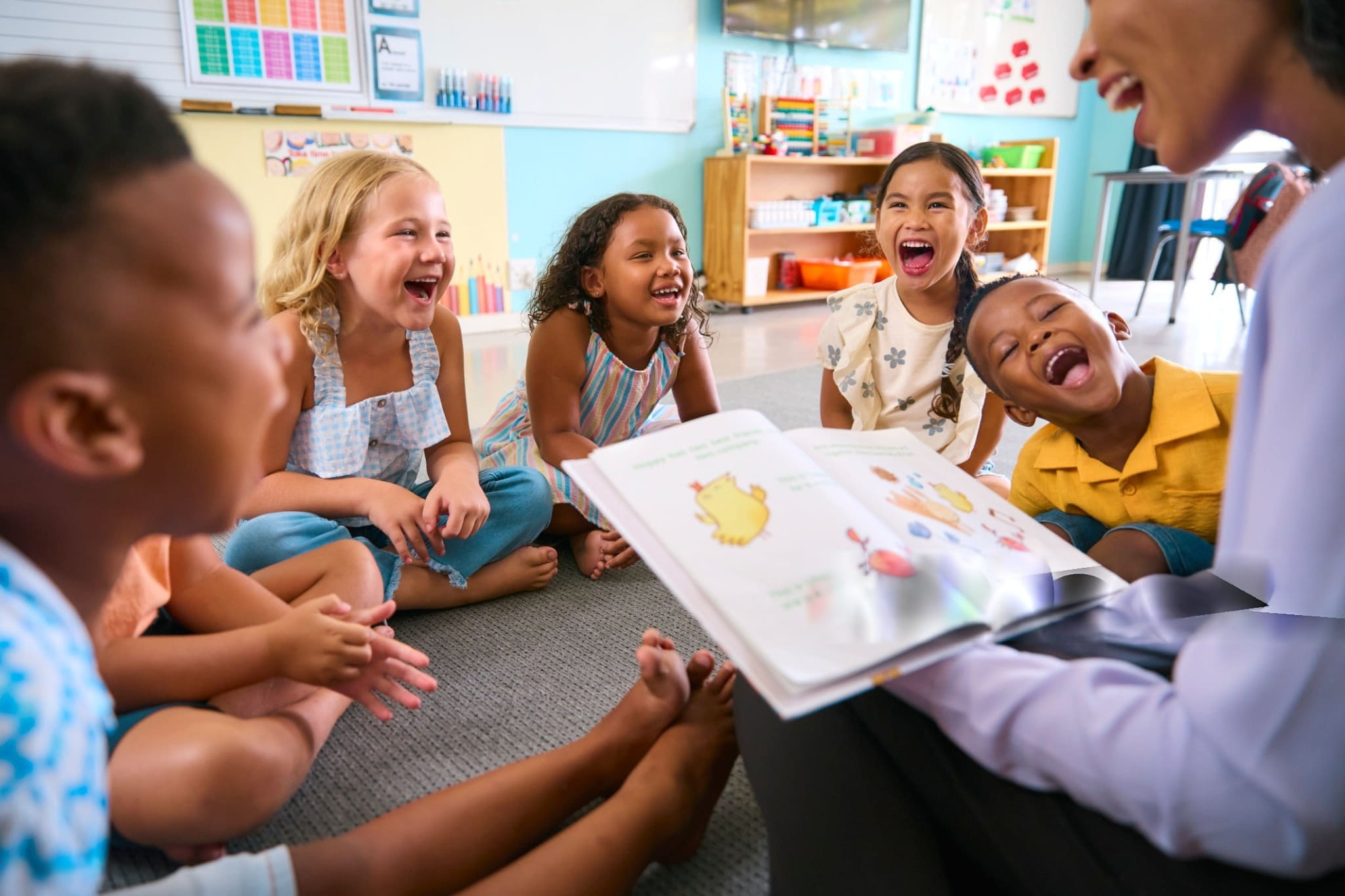 Respire Education | A teacher reading a colorful book aloud to a group of laughing young children sitting on the classroom floor.