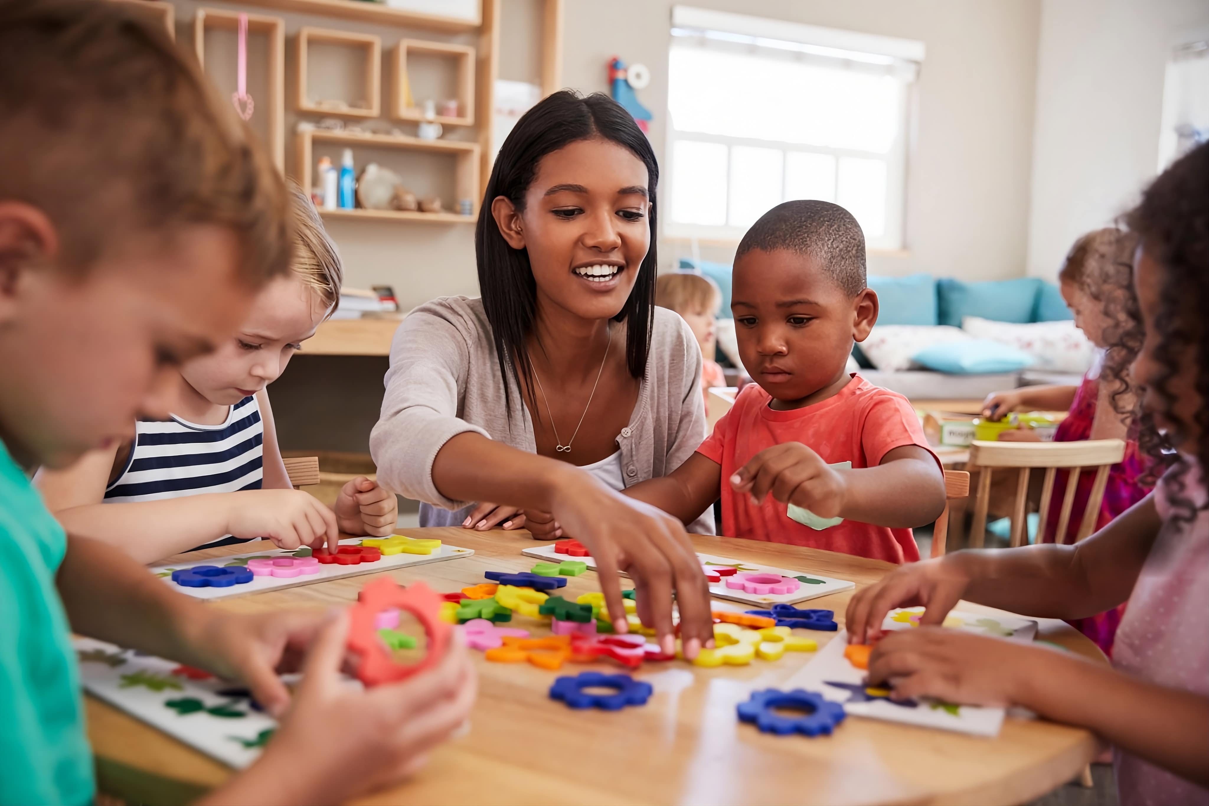 Respire Education | Teacher and diverse children sitting at a table sorting colorful flower-shaped pieces in a classroom.