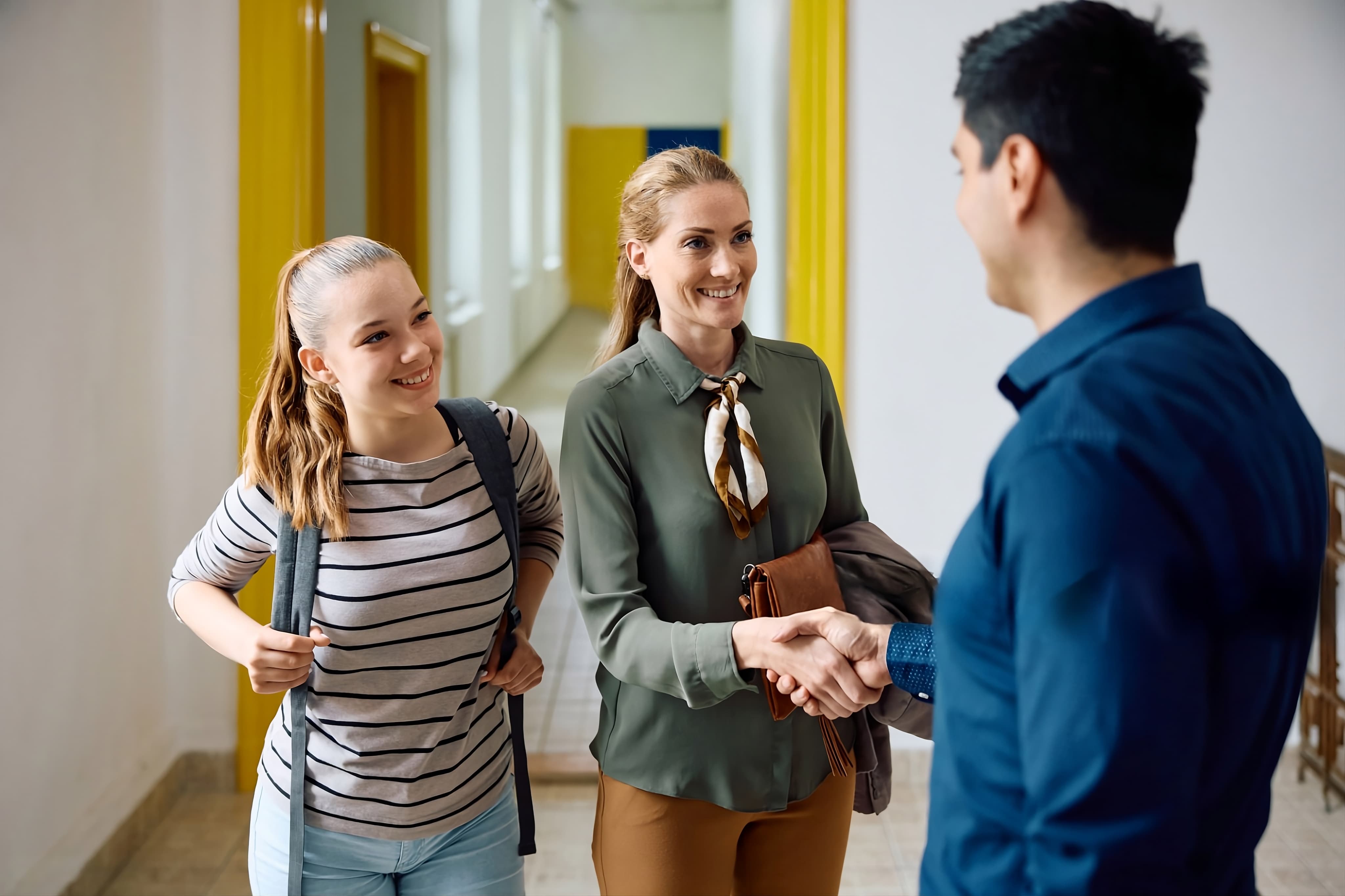 Respire Education | Two women smiling and greeting a man with a handshake in a bright hallway.