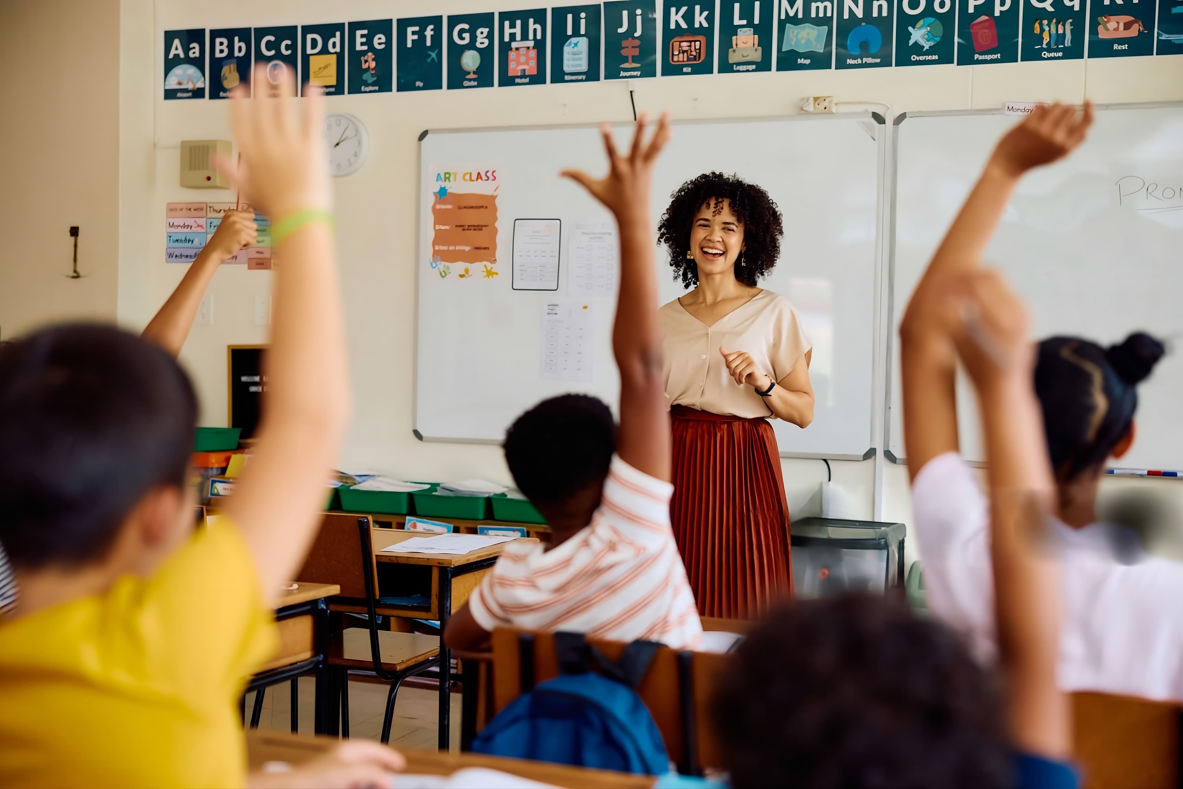 Respire Education | Teacher smiling at students raising hands in a classroom with alphabet posters.