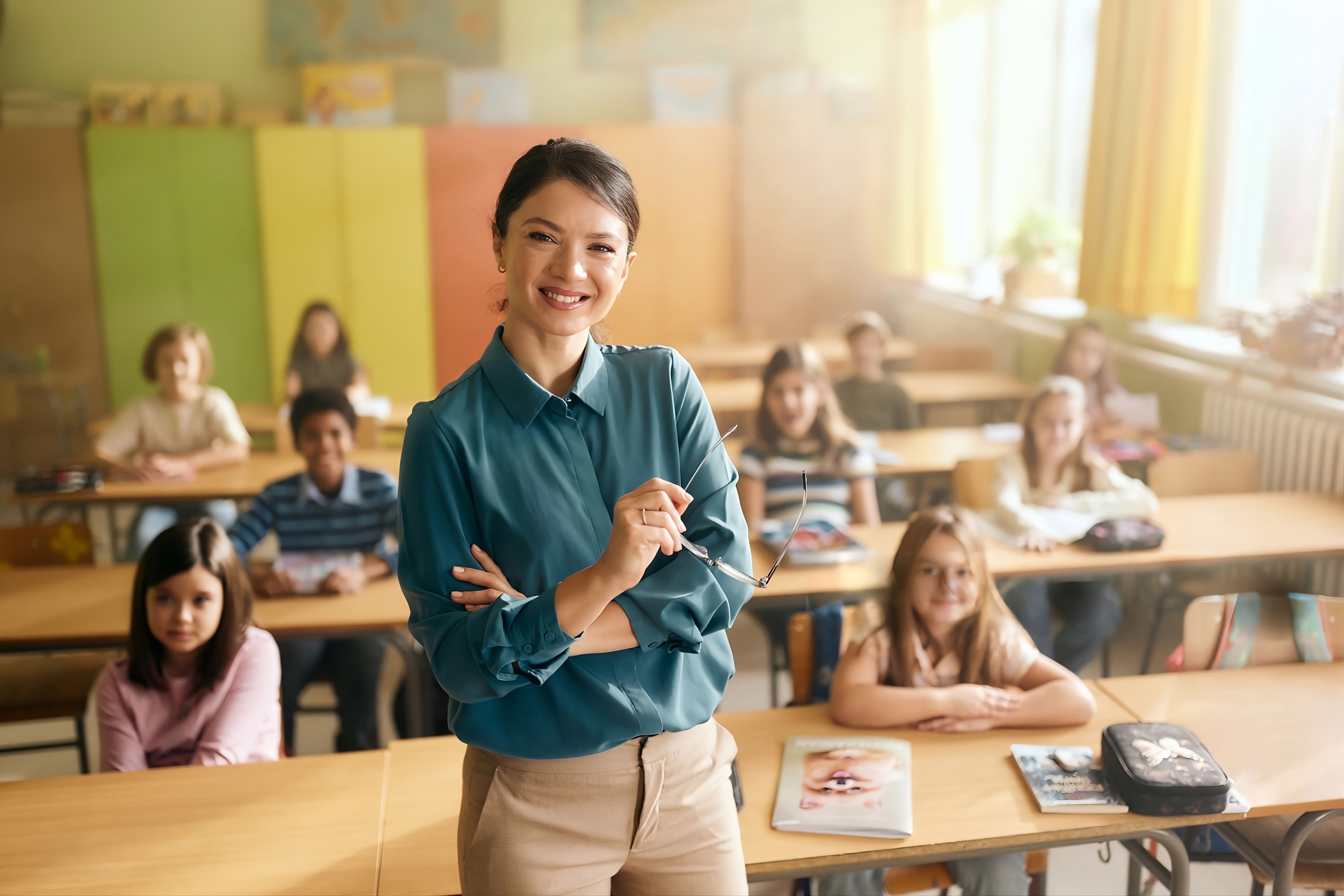 Respire Education | Smiling female teacher holding glasses in front of a classroom with seated young students.