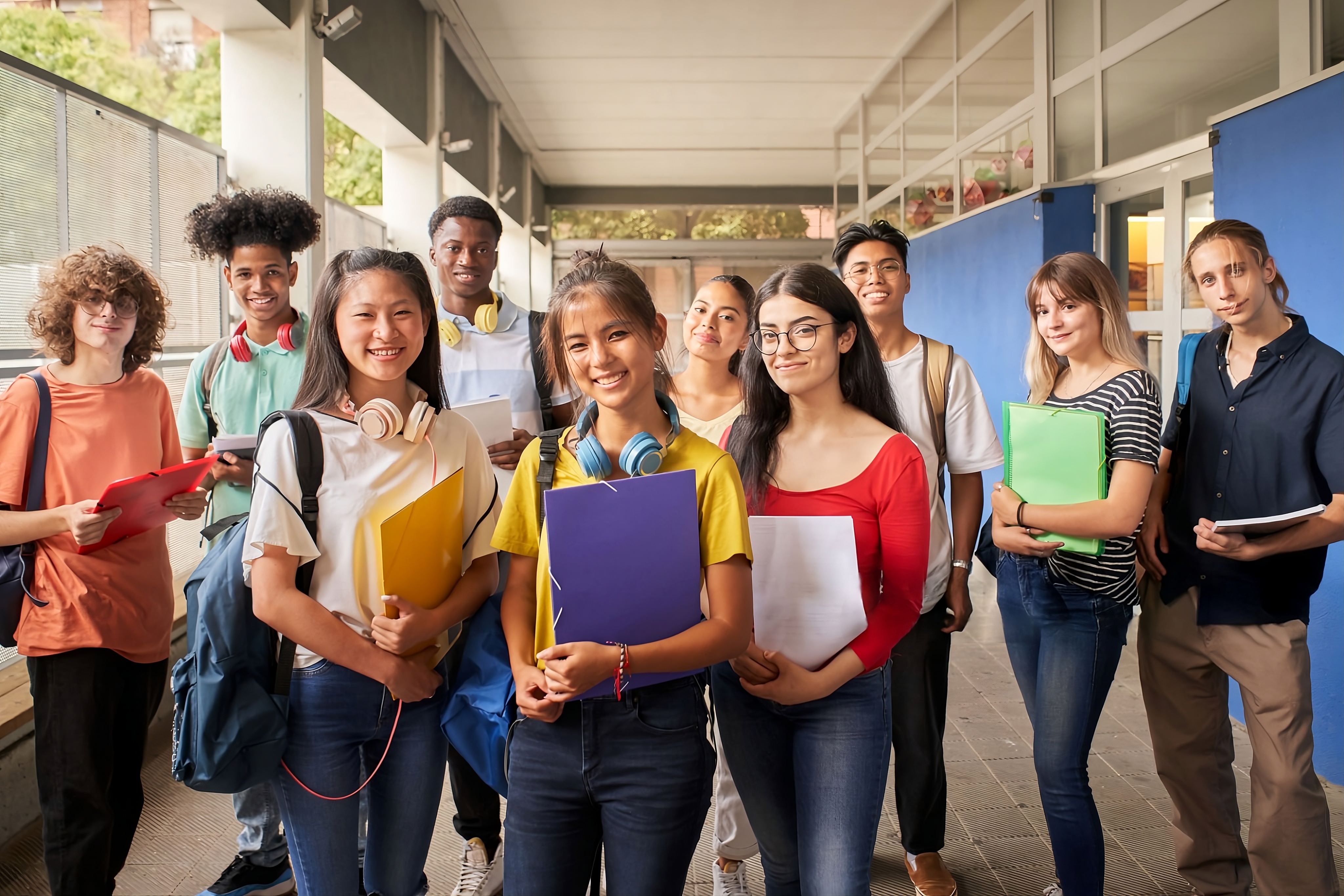 Respire Education | Diverse group of smiling high school students standing in a school hallway holding notebooks and folders.