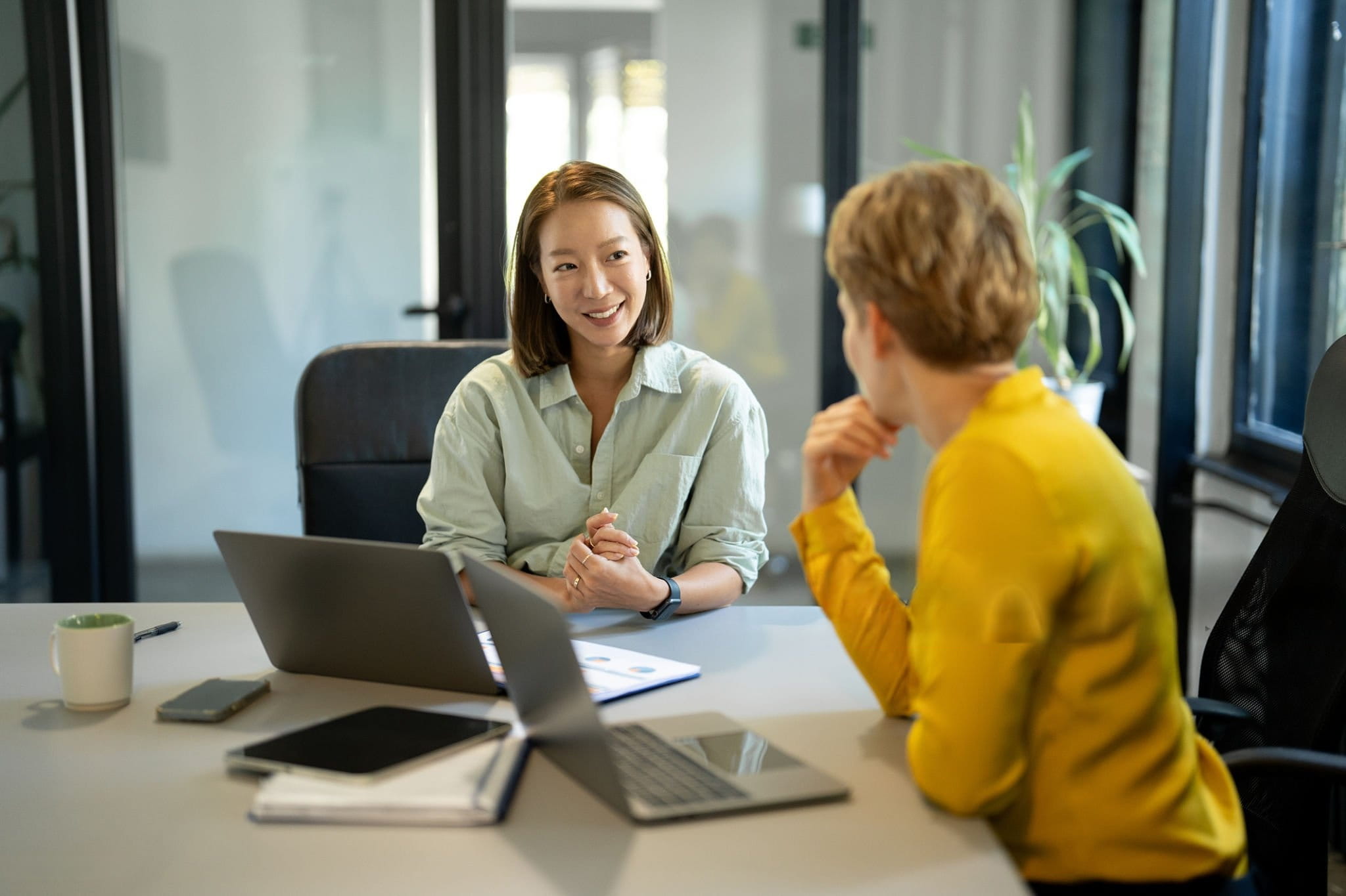 Respire Education | Two colleagues in a modern office having a conversation across a desk with laptops and documents.