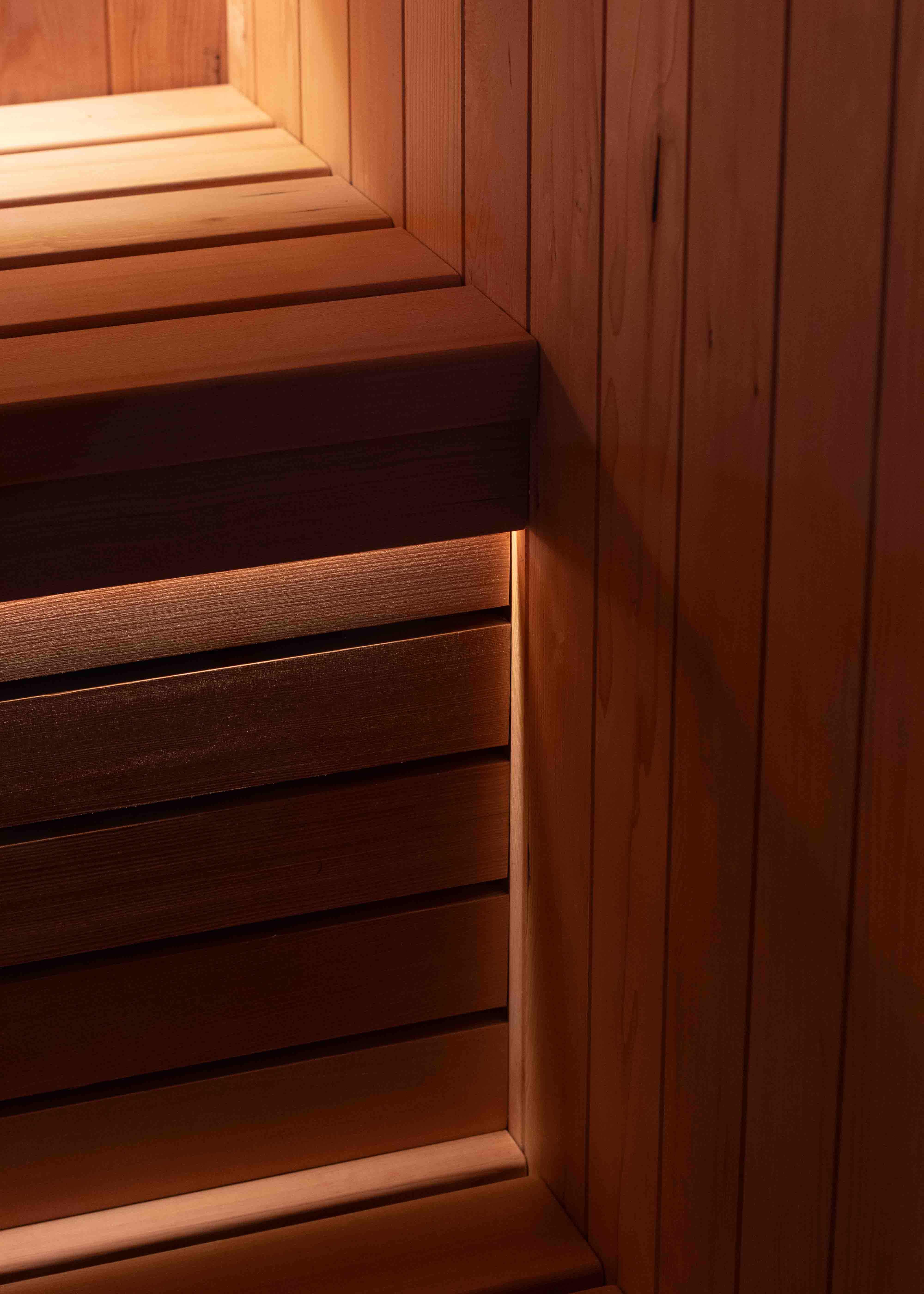 Interior of a wooden sauna with tiered benches, backrest, lighting, and a heater with sauna stones.