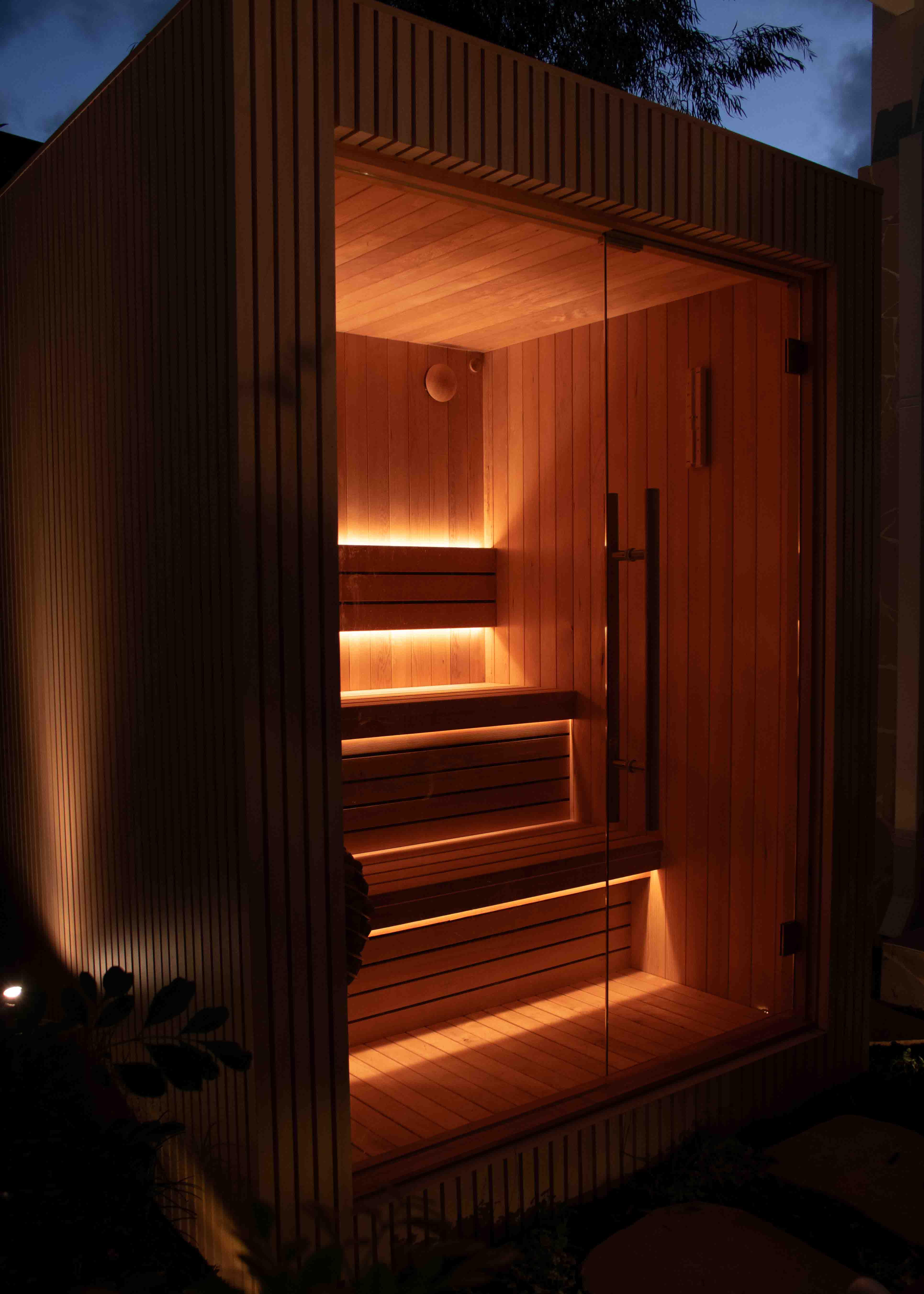 Interior of a custom sauna with glass door and wooden handle.
