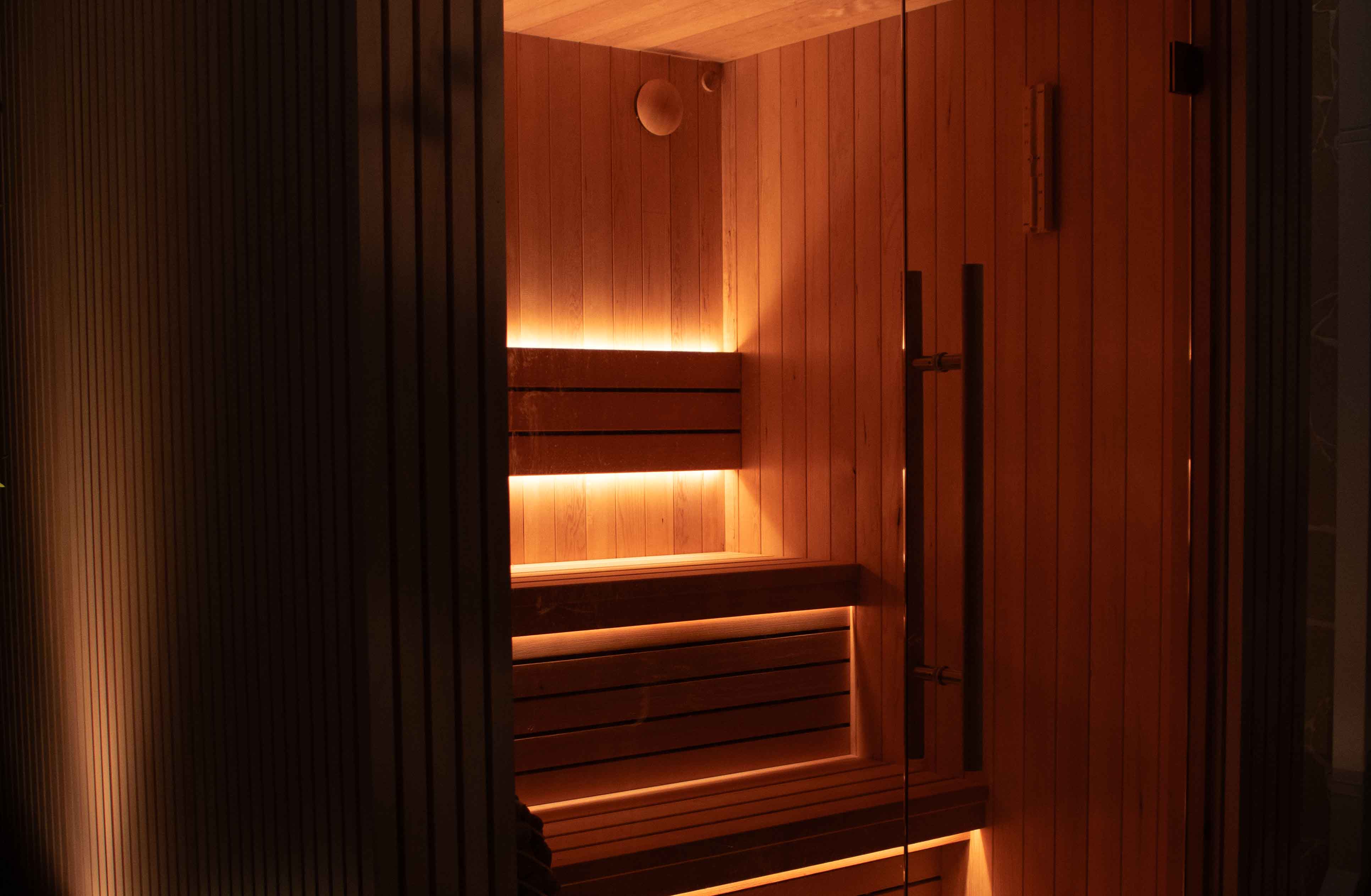 Interior of a custom wooden sauna lit by warm lighting highlighting custom benches and walls.