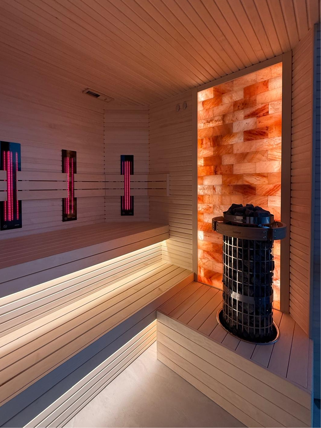 Interior of custom perth-made wooden sauna with multi-level benches and a heater filled with stones.