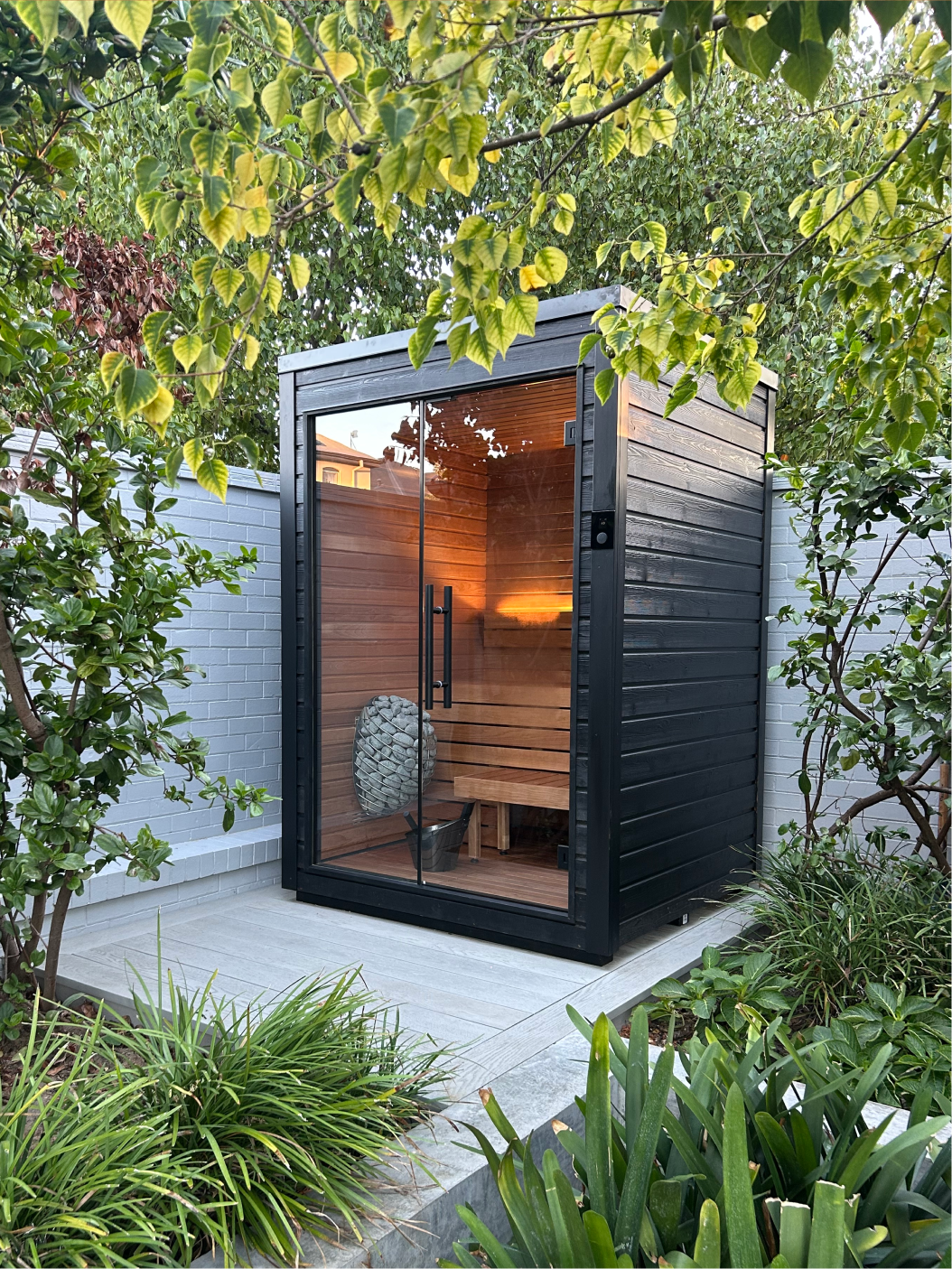 Interior of a wooden sauna with tiered benches, backrest, lighting, and a heater with sauna stones.