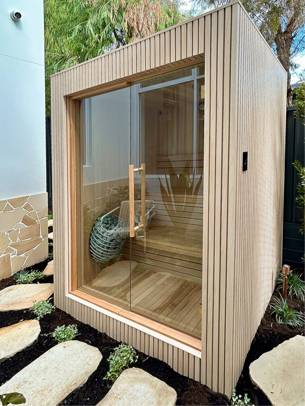 Interior of custom perth-made wooden sauna with multi-level benches and a heater filled with stones.