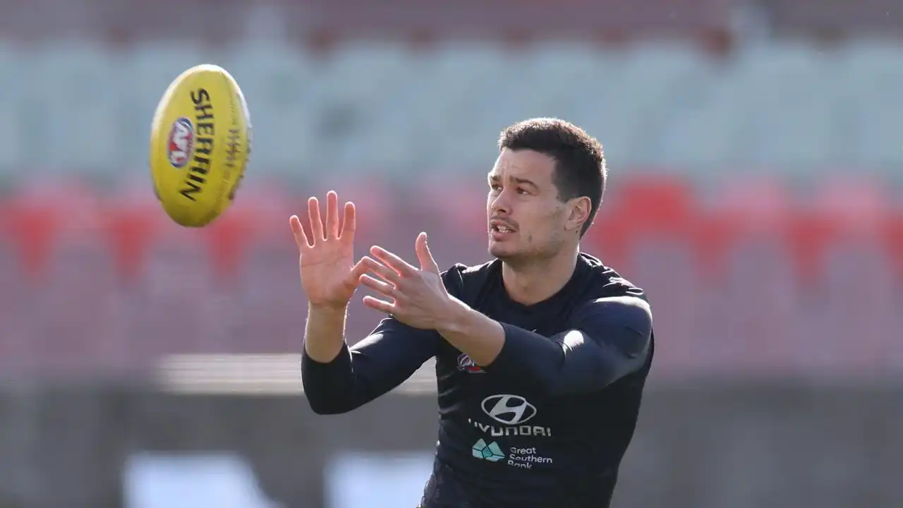 A man in black sportswear reaching out to catch a yellow Sherrin football mid-air.