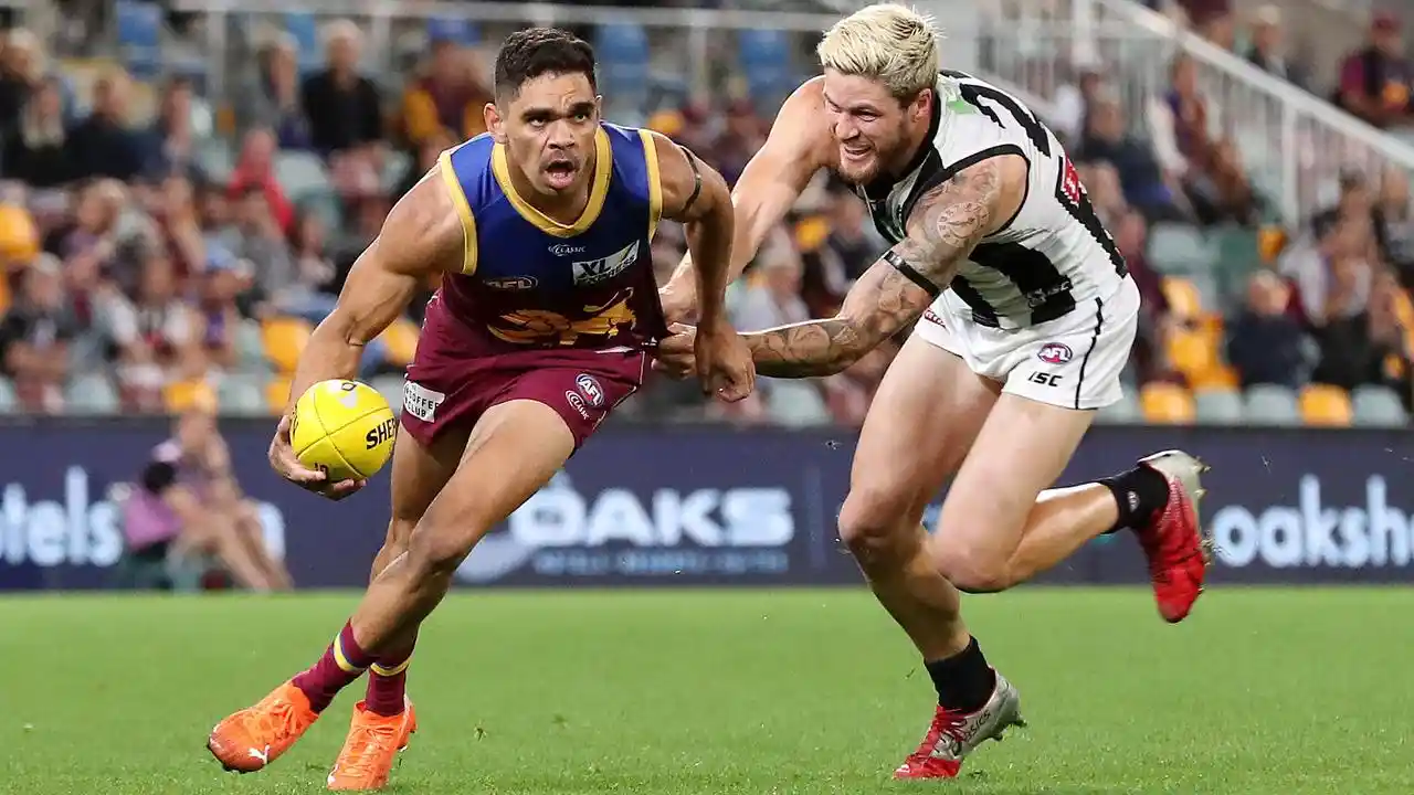 Australian football player evades tackle while running with the ball on grass field during match.