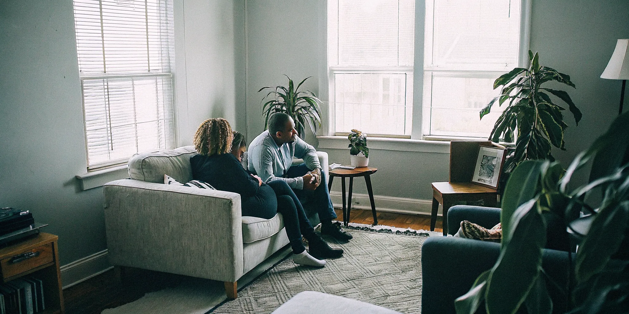 A couple sitting on a couch in a bright therapy office speaking with a counselor