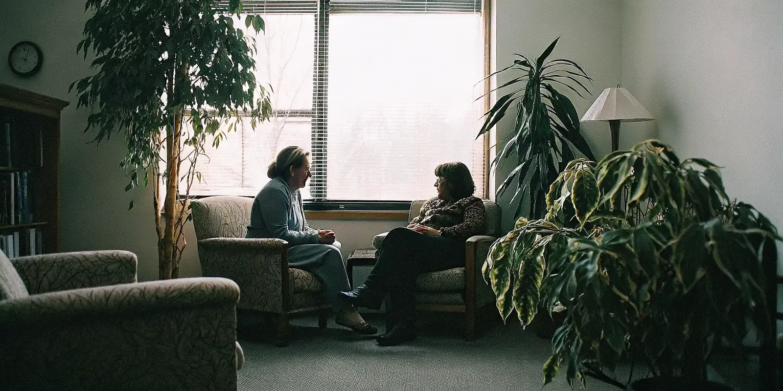 A multilingual therapist speaking with an adult client in a warm, professional counseling office with soft natural light