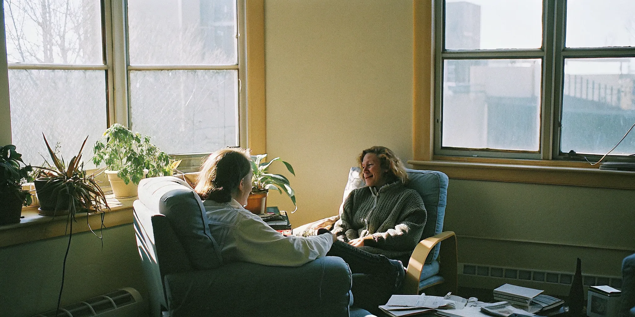 A counselor in a calm sunlit office talking with an adult client in a supportive therapy session