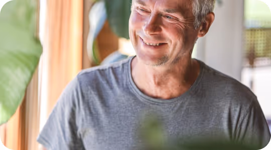 Homme souriant portant un t-shirt gris parmi des plantes d'intérieur vertes.