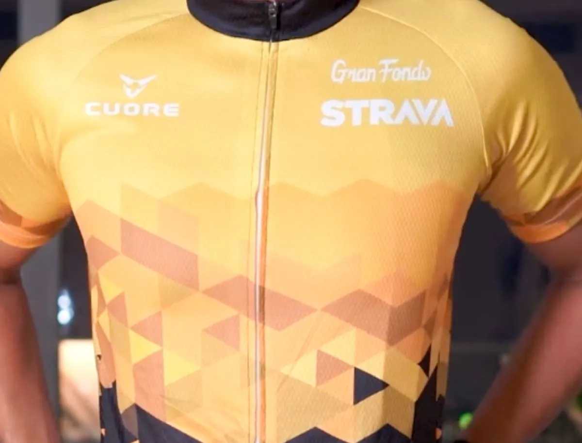 Closeup front view of a yellow and black Cuore x Strava Gran Fondo cycling jersey showing geometric triangle pattern, Cuore logo, and Gran Fondo Strava branding on the chest