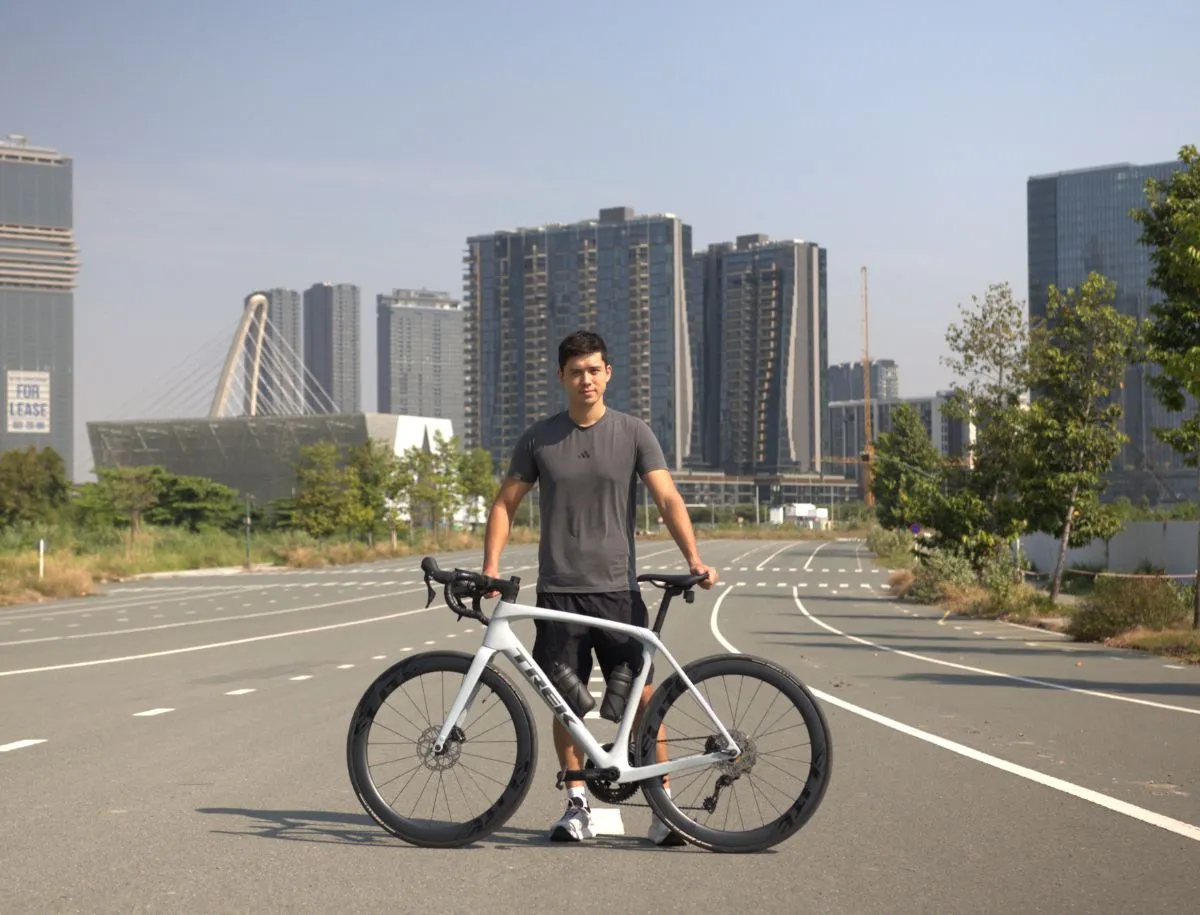 Cyclist Mike Dee standing with a white Trek Domane SL5 disc road bike fitted with Elitewheels ENT 2.0 50mm carbon wheels on an open urban road