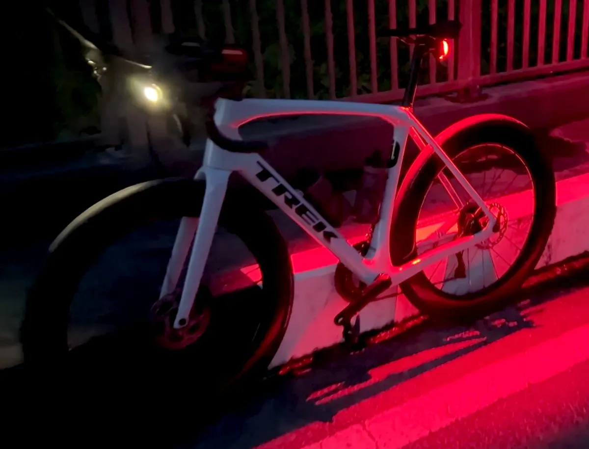 White Trek road bike photographed at night with Magicshine HORI 900 front light illuminated on the handlebars casting a bright white beam, and Magicshine Seemee 200 V2.0 red rear light glowing on the seatpost, showing a complete front and rear Magicshine lighting setup for night road cycling