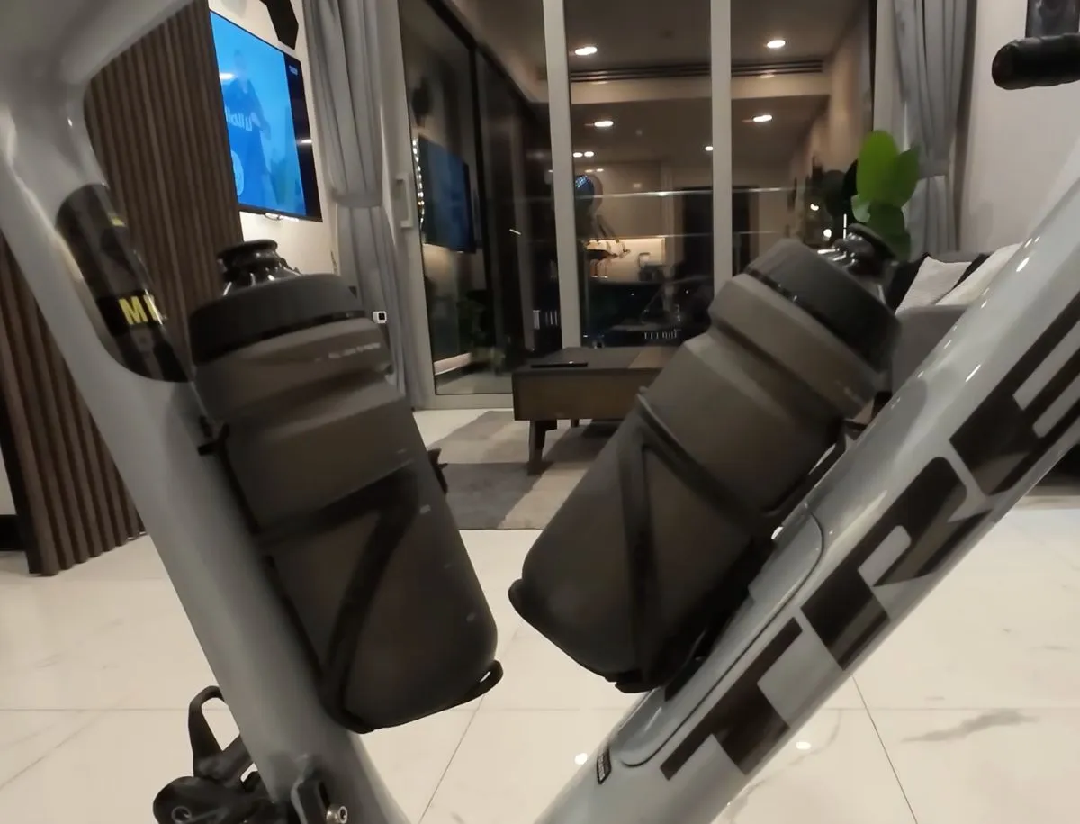 Close-up view of two Topeak Ninja Cage Z water bottle holders mounted on the frame and seat tube of a Trek road bike, each holding a Topeak 650ml cycling water bottle, photographed indoors showing the dual hydration setup from the rider's perspective