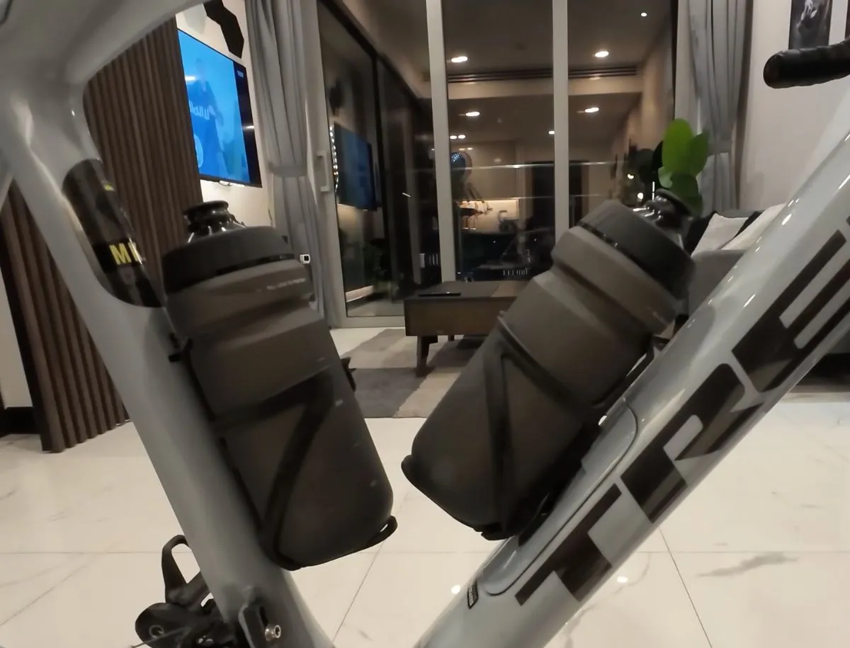 Two black water bottles secured in cages mounted on the down tube and seat tube of a Trek road bike frame indoors