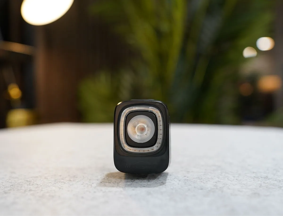 Close-up front view of the Magicshine SEEMEE 200 v3.0 bike rear light showing the central COB LED lens surrounded by a ring of smaller SMD LEDs in a black housing, placed on a concrete surface