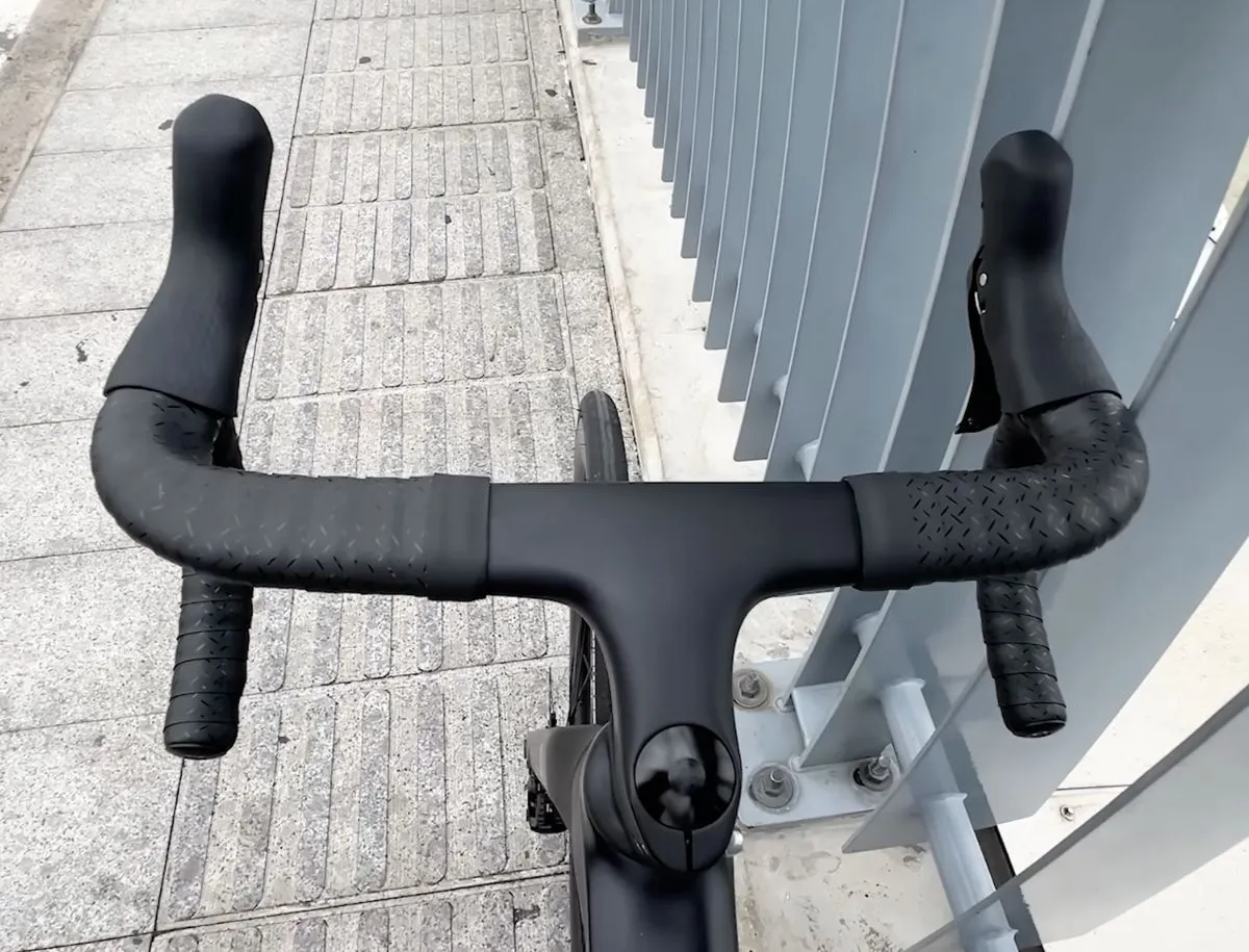 Top-down view of SAVA A7L Pro integrated carbon handlebar and stem unit showing textured bar tape with diamond grip pattern, internal cable routing ports, and Garmin computer mount in the center