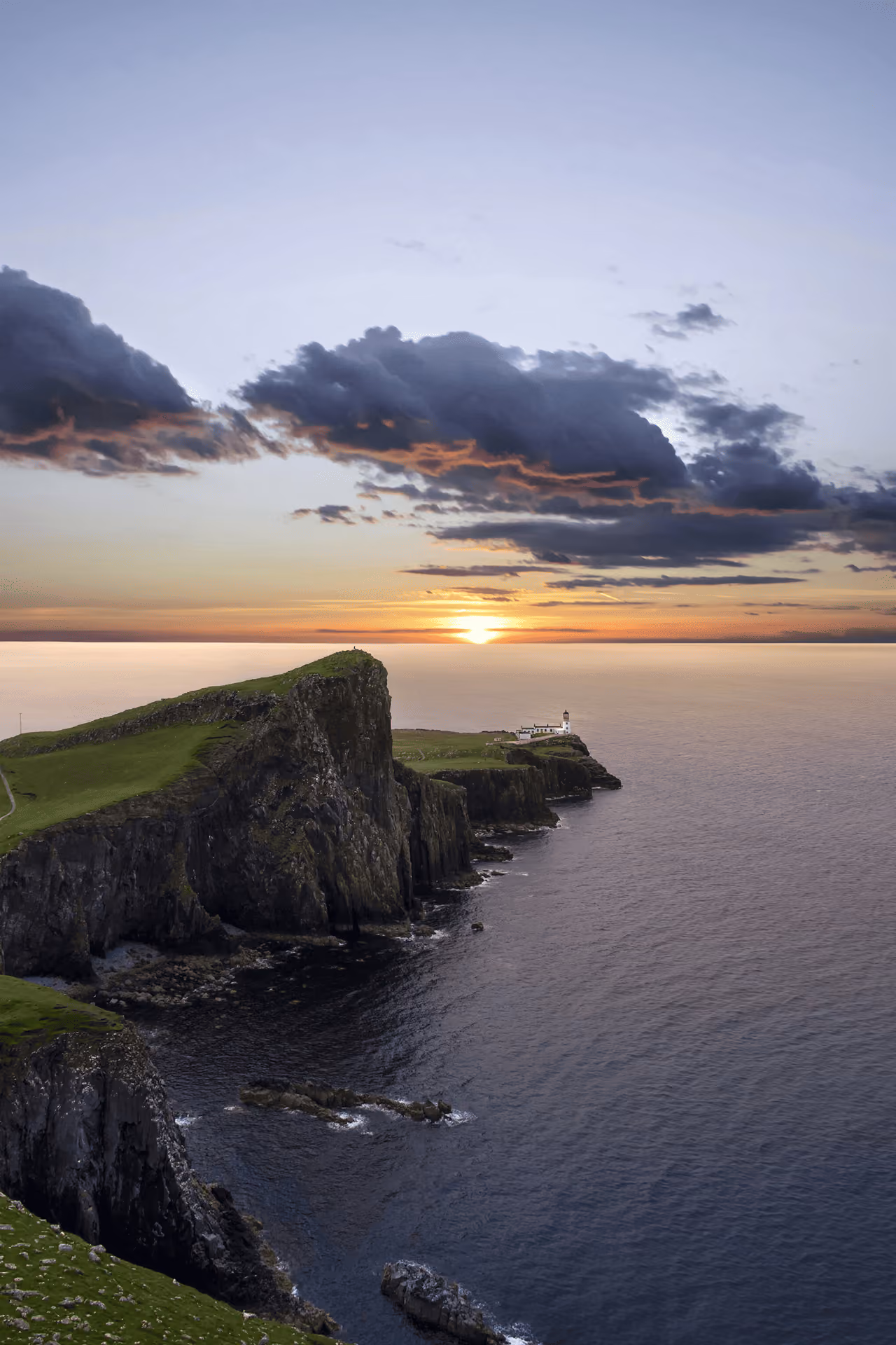 Neist Point lighthouse on a rugged clifftop overlooking calm sea at sunset