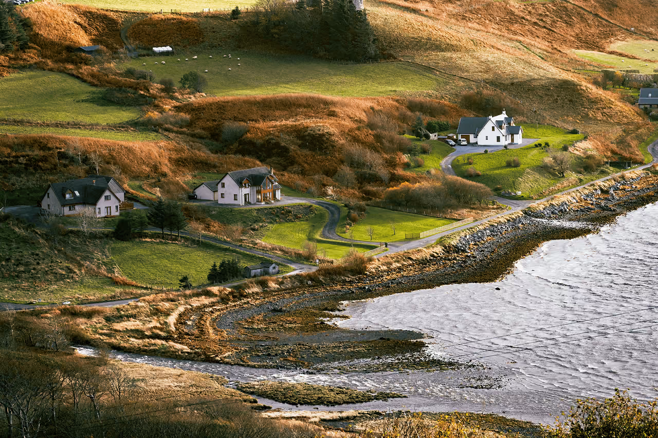 Aerial view of scattered cottages along a quiet Skye coastline with rolling hills