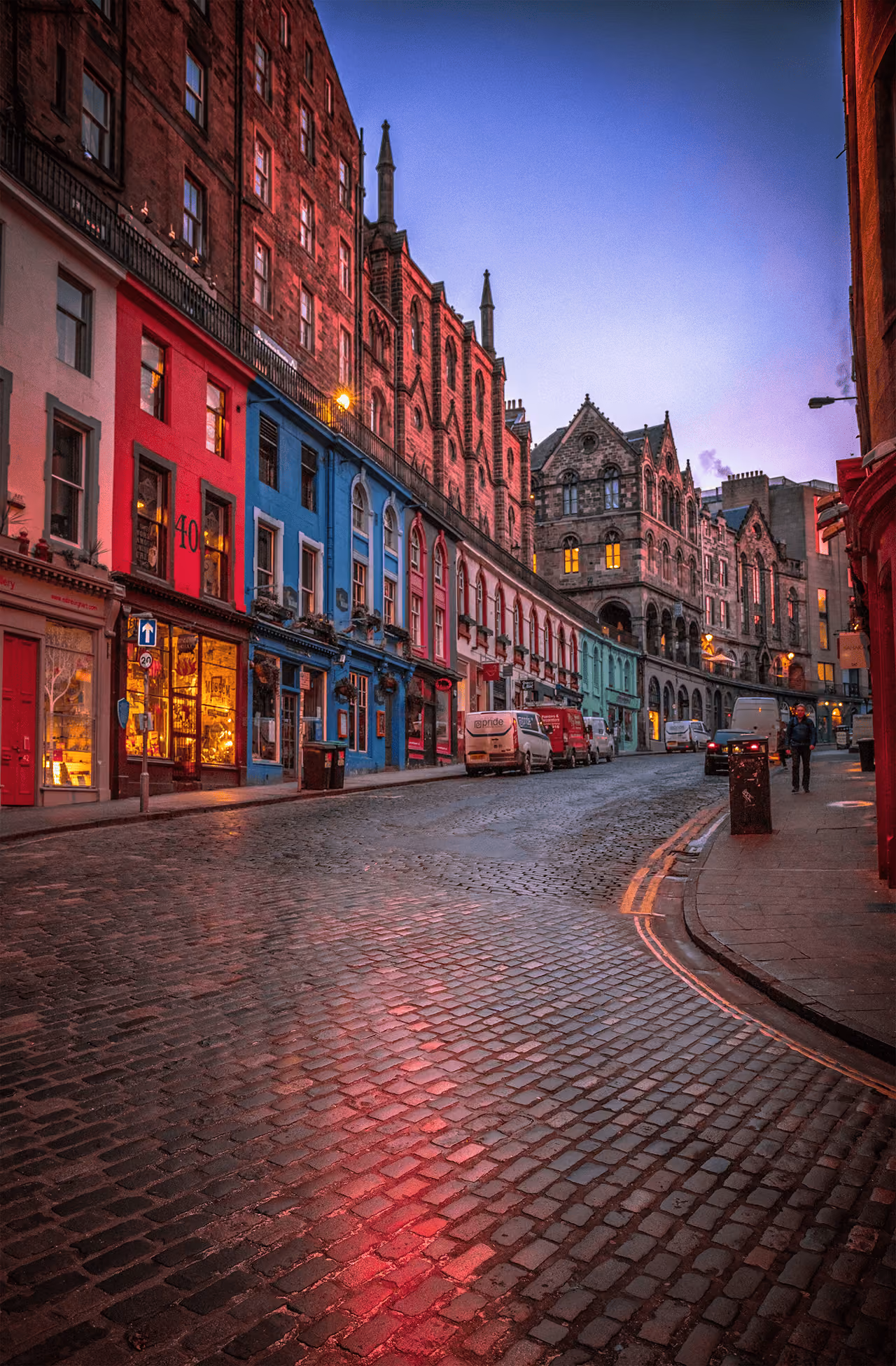 Colourful curved shopfronts of Victoria Street at dawn with wet cobblestones reflecting the lights