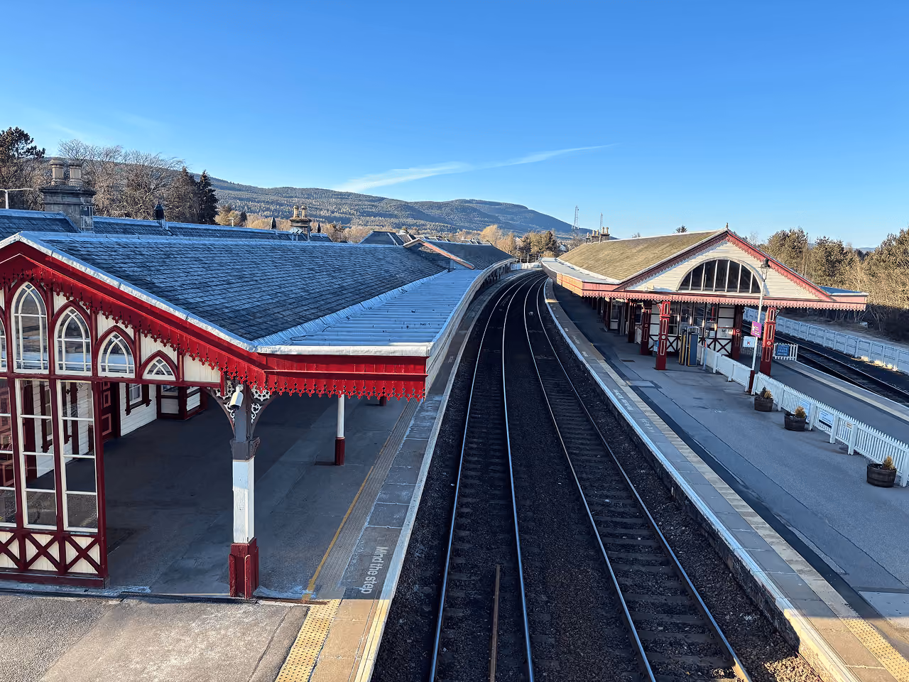 Aviemore's red and white Victorian railway station building curving alongside empty tracks under a deep blue winter sky