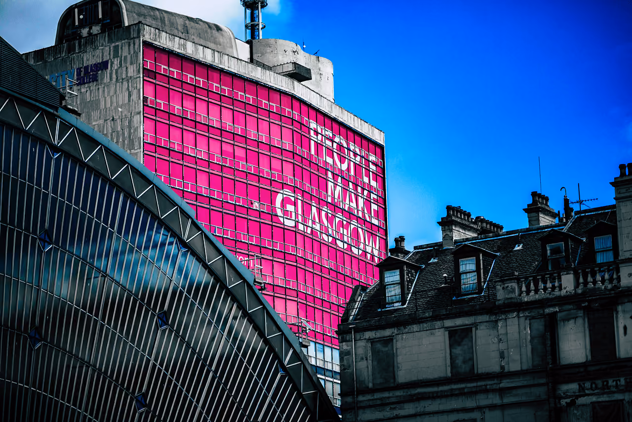 The bold pink 'People Make Glasgow' slogan displayed across a building facade above the curved glass roof of Glasgow Queen Street station