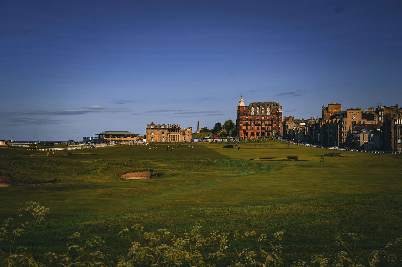 The fairways of St Andrews Old Course at golden hour with the R&A clubhouse and Rusacks Hotel glowing in warm evening light