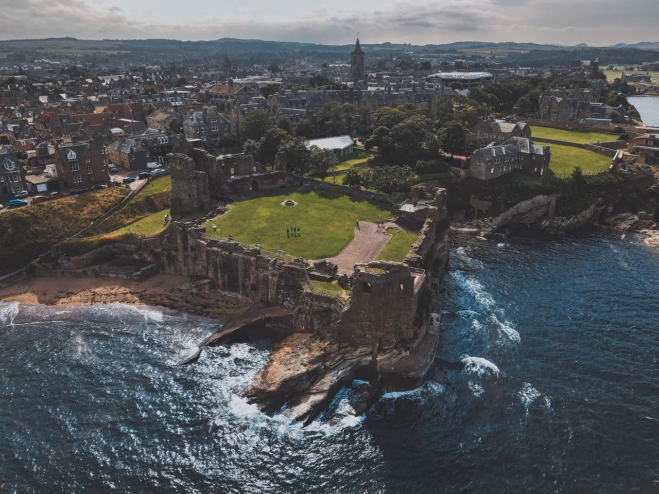 Aerial view of St Andrews Castle ruins perched dramatically on a clifftop promontory with waves breaking against the rocks below