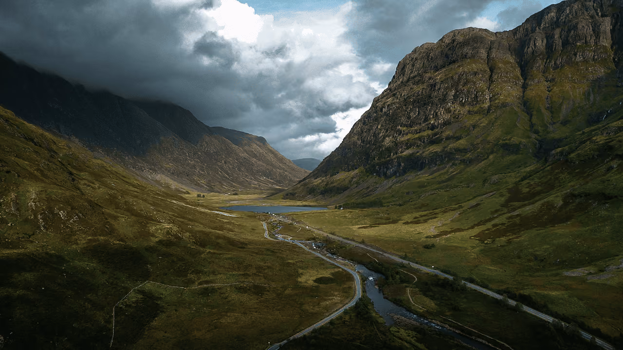 Aerial view down the Glencoe pass with the A82 road and river winding between towering mountains under a brooding sky