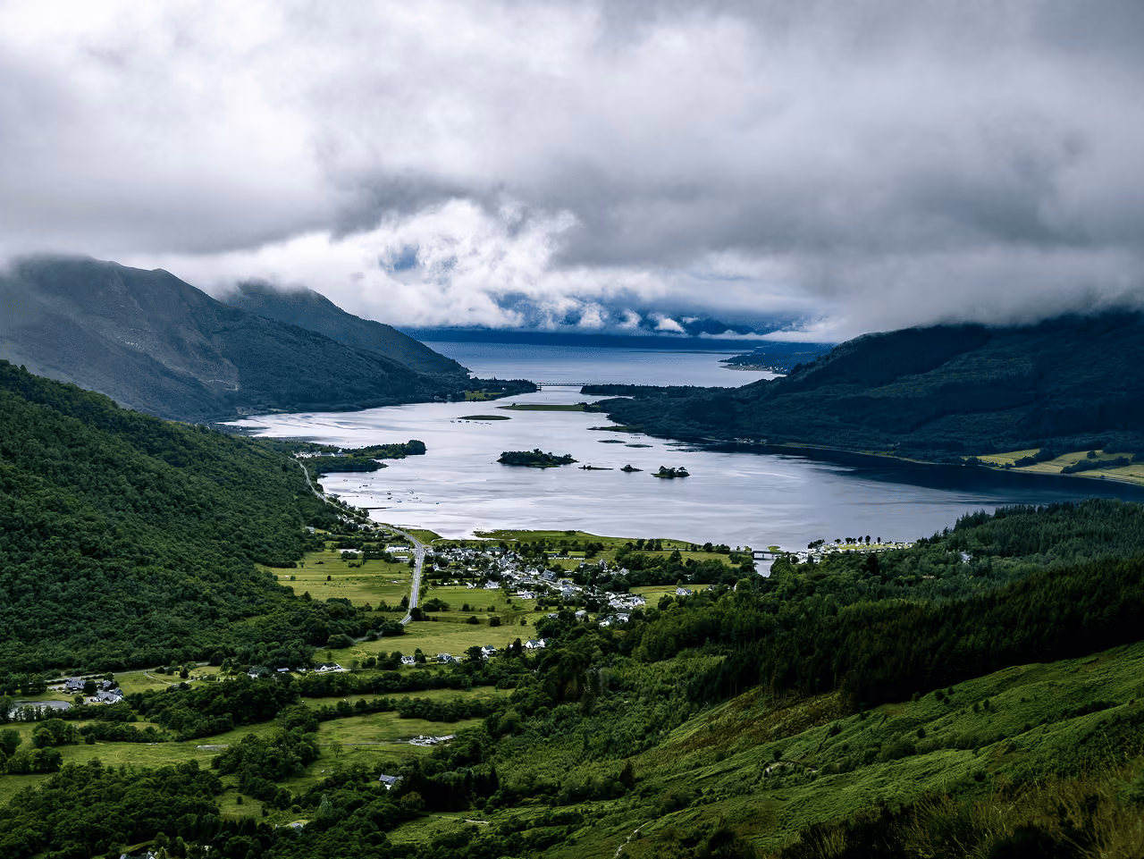 Aerial view of Loch Leven and the village of Glencoe nestled in the valley below dark storm clouds rolling over the mountains