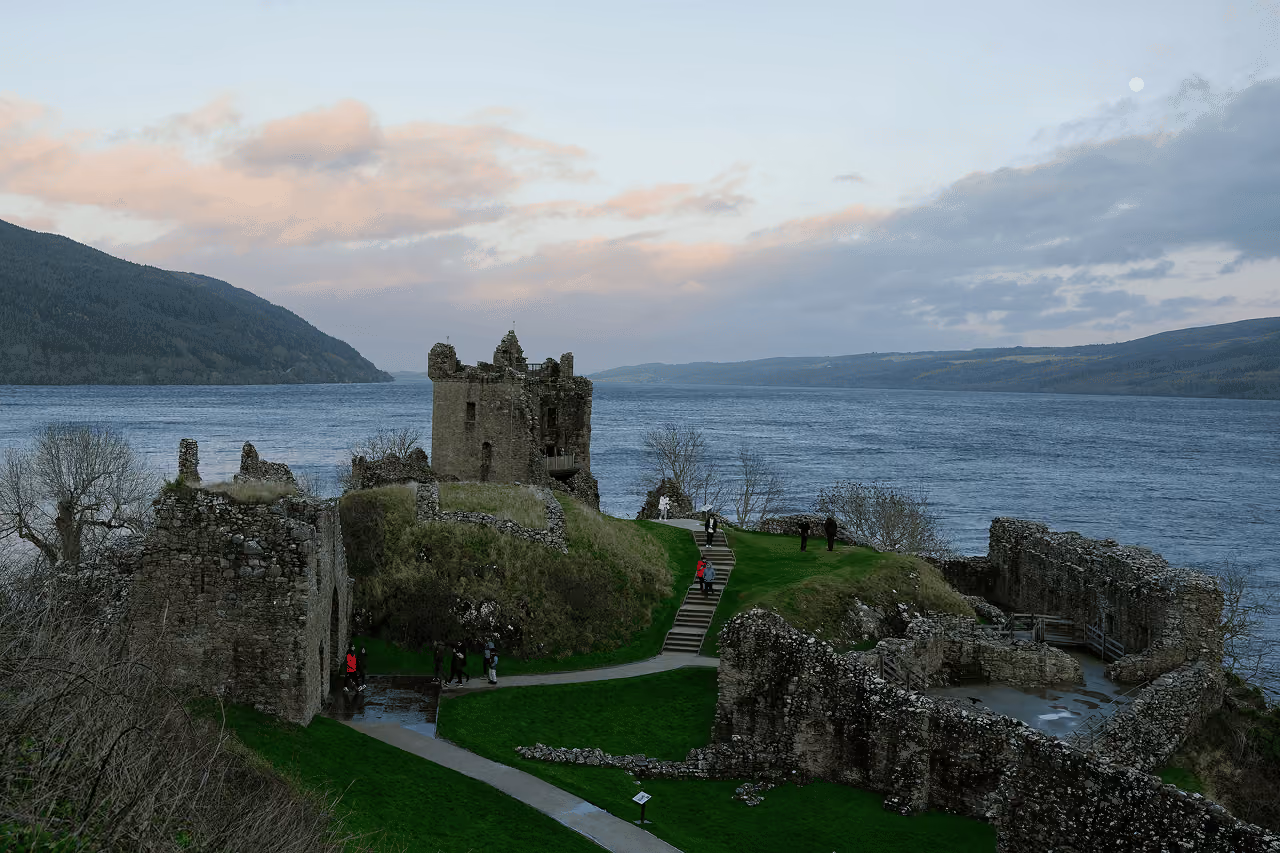 Urquhart Castle's tower house silhouetted against a pastel dusk sky above the still waters of Loch Ness with a full moon rising