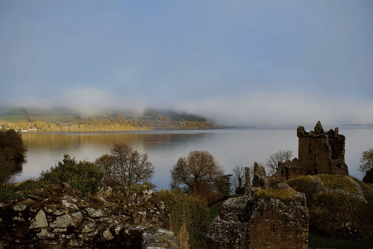 Urquhart Castle ruins on the shore of Loch Ness on a misty autumn morning with low cloud drifting across the still calm water