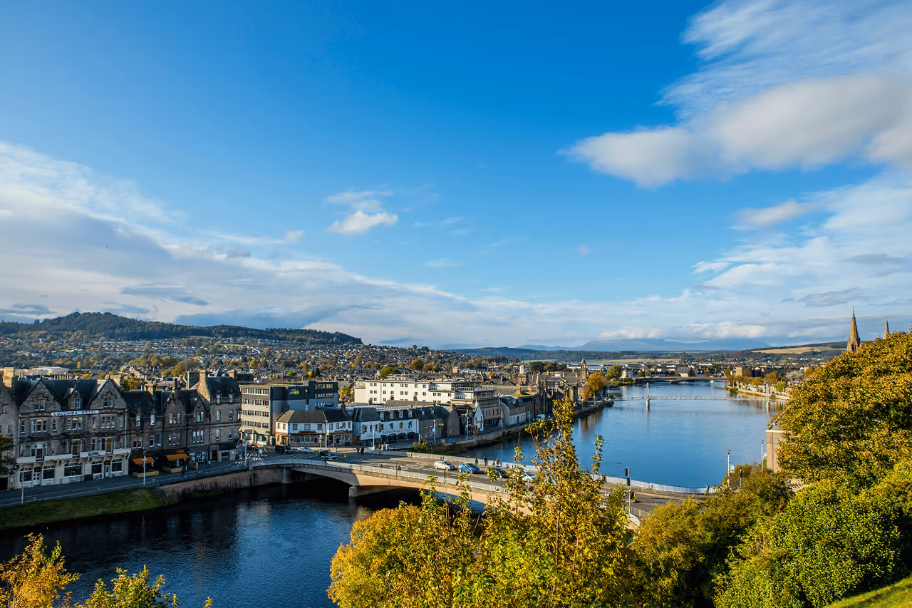Panoramic view of Inverness city centre with the River Ness, a stone bridge and the Columba Hotel in warm autumn light with mountains stretching to the horizon