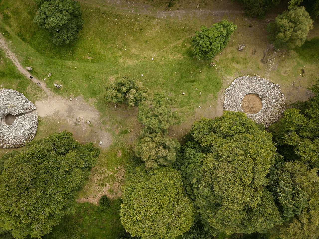 Aerial view of two prehistoric stone cairns at Clava Cairns set in green grass and summer woodland near Inverness