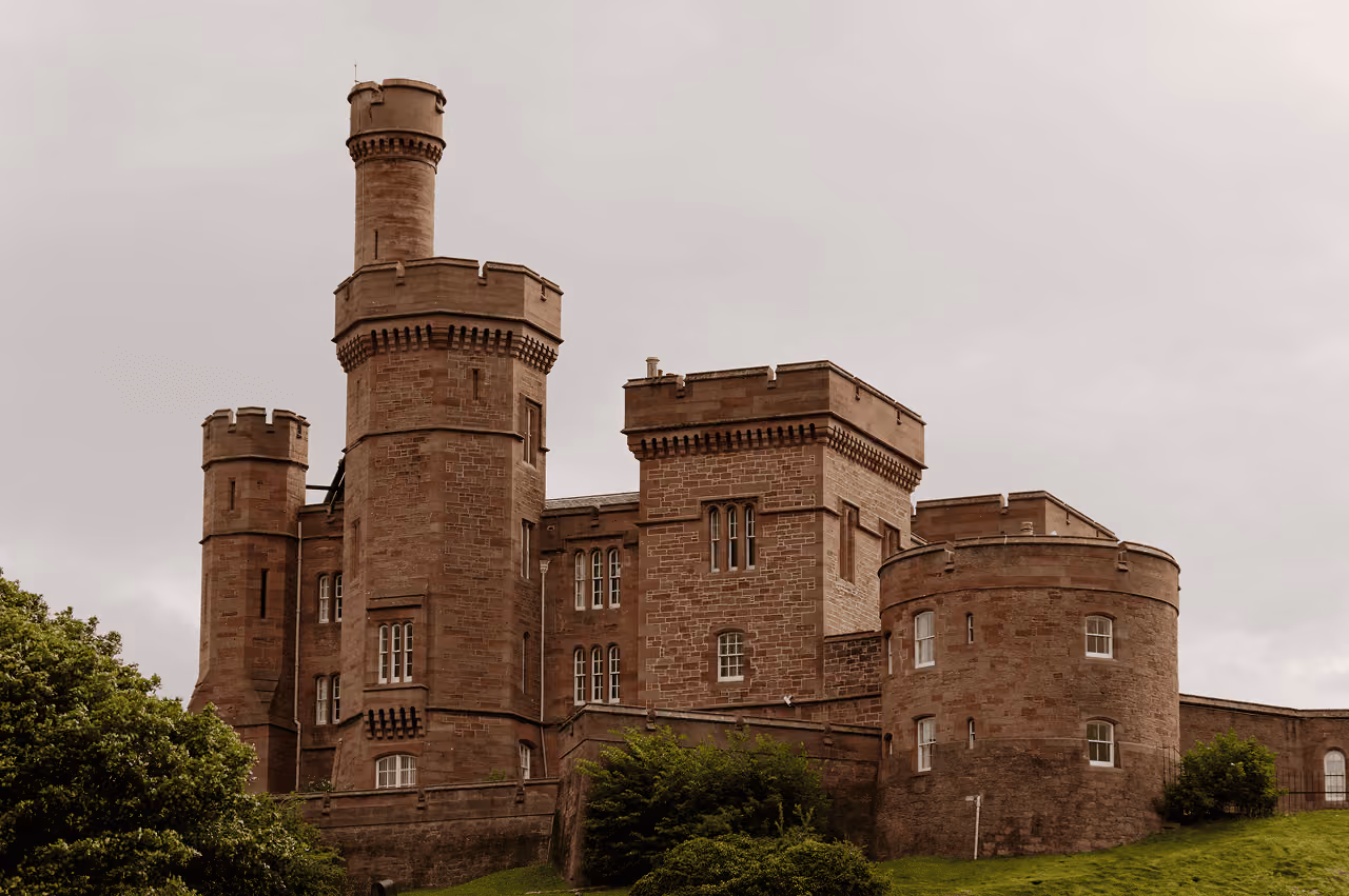 Inverness Castle's red sandstone towers and crenellated battlements rising against an overcast sky above green trees