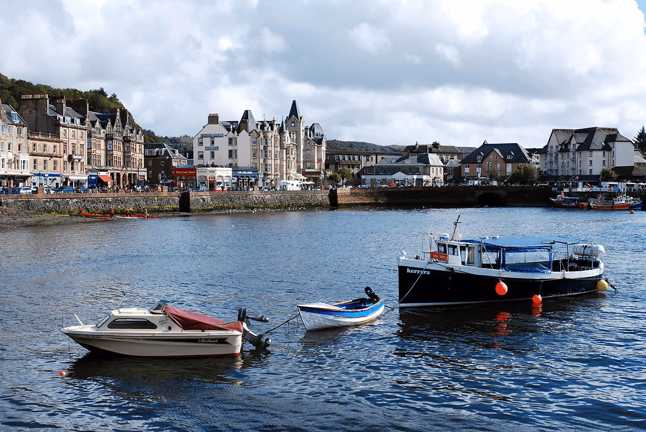 Colourful fishing boats moored in Oban harbour with the town and hillside rising behind them