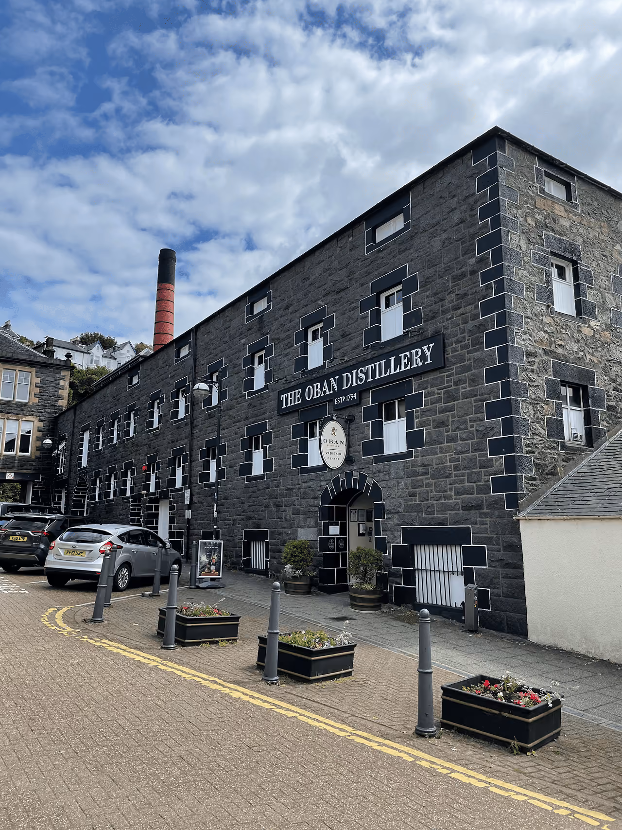 Oban Distillery stone facade in the heart of town with a lamp post in the foreground under grey skies
