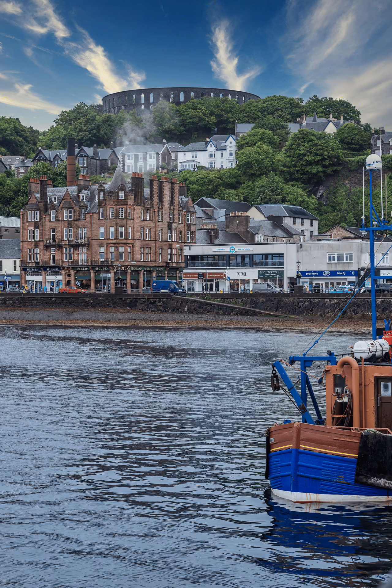 Oban seafront looking up to McCaig's Tower crowning the hill above the town with boats in the harbour below