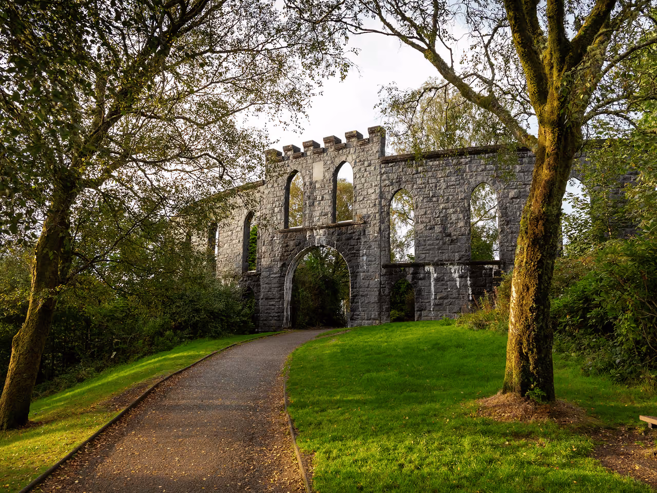 Path leading through McCaig's Tower stone arch gateway surrounded by trees and lawns on a misty autumn day