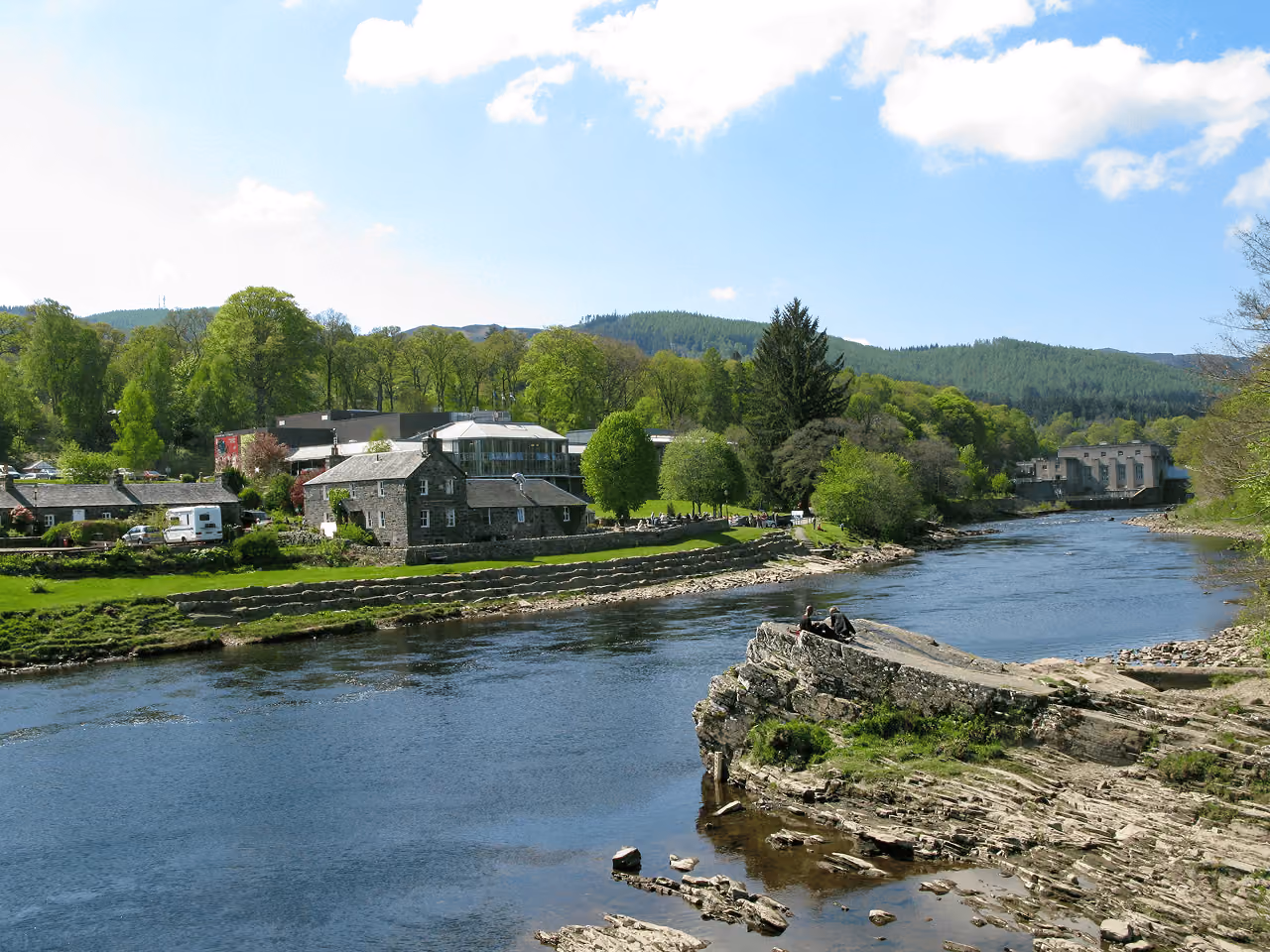 The River Tummel flowing through Pitlochry with green spring trees and the Pitlochry Festival Theatre behind