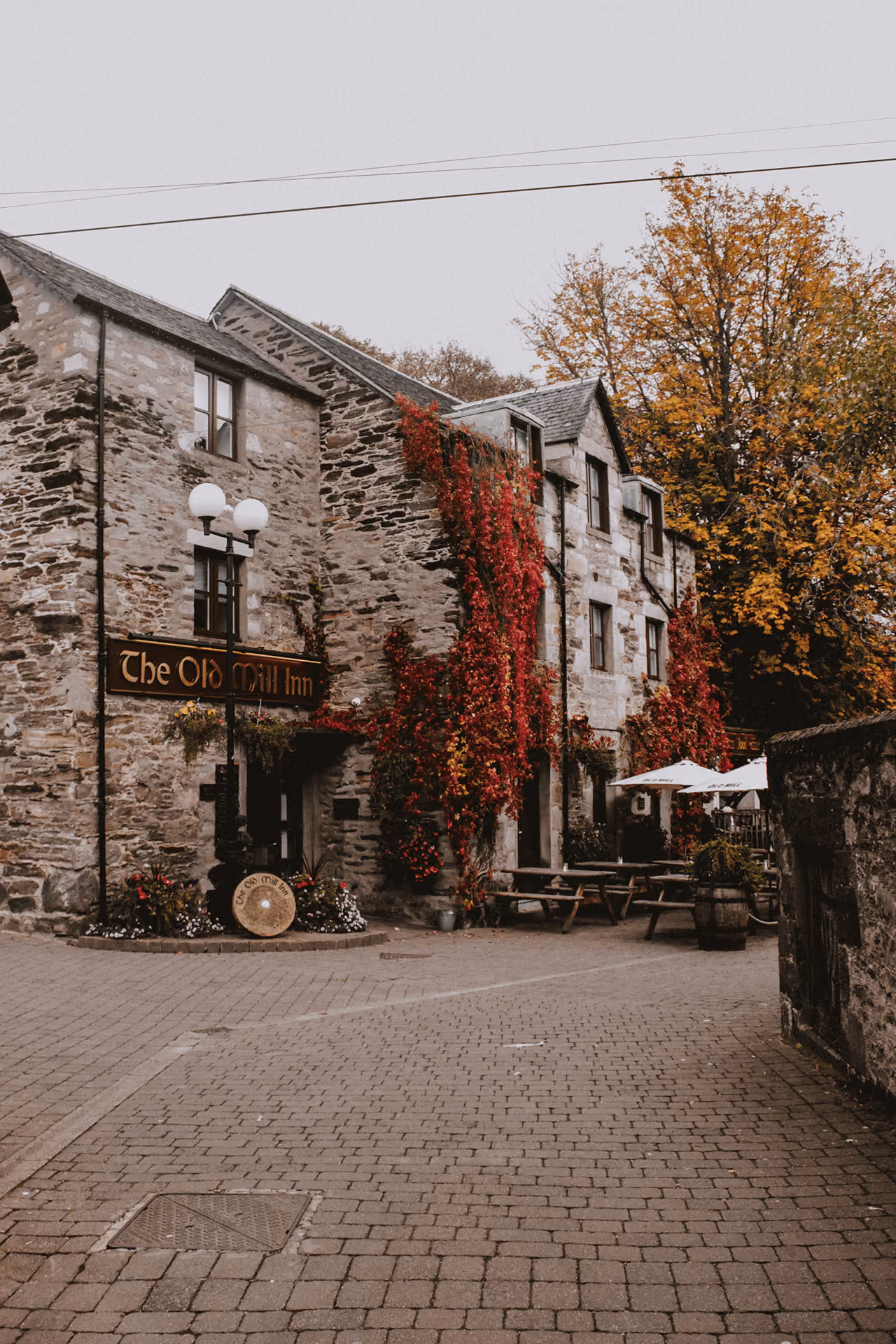 The Old Mill Inn stone pub covered in vibrant red ivy with autumn trees and outdoor seating on a cobbled courtyard